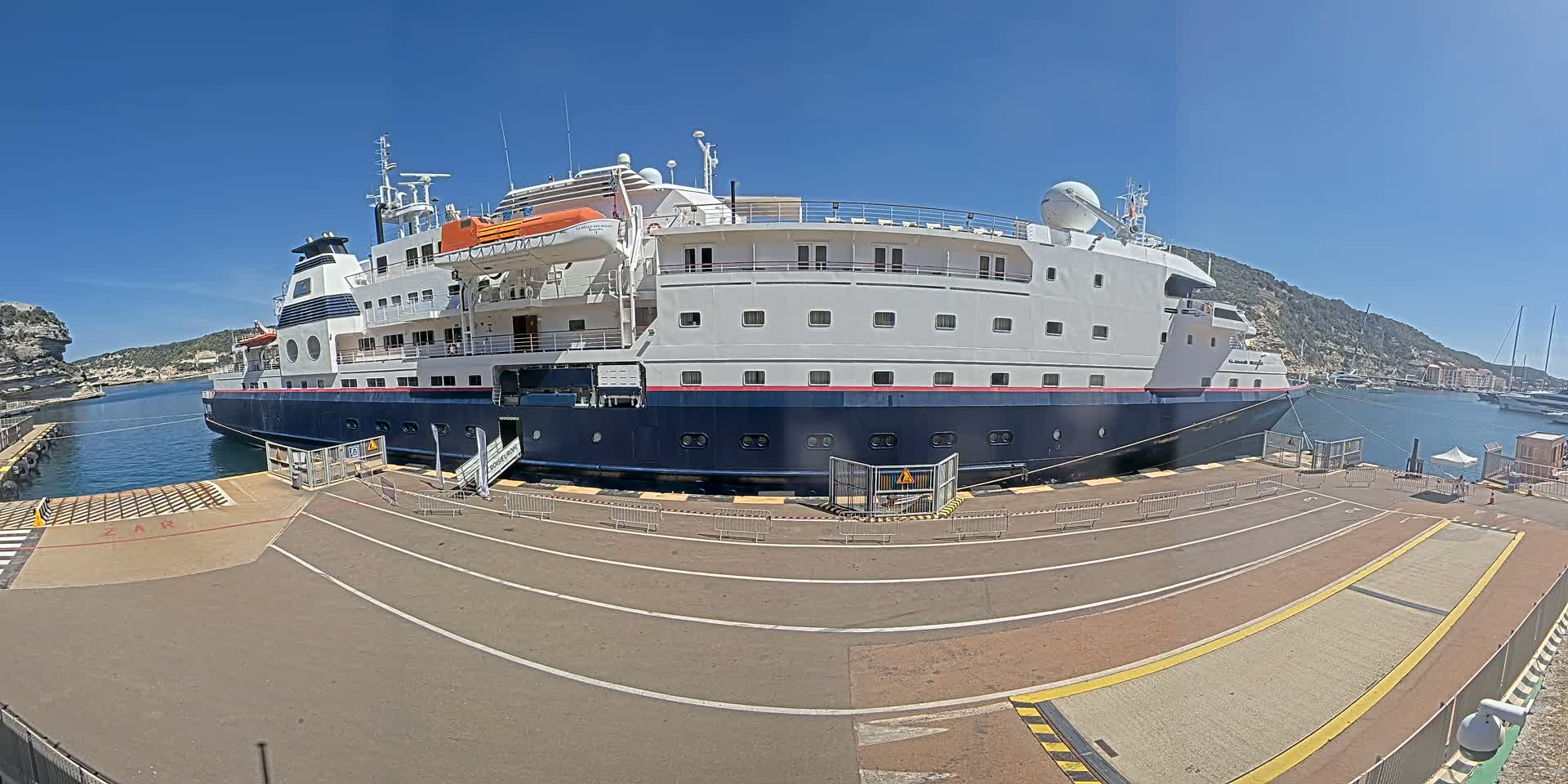 A large, white and blue cruise ship is docked at a port on a sunny day.