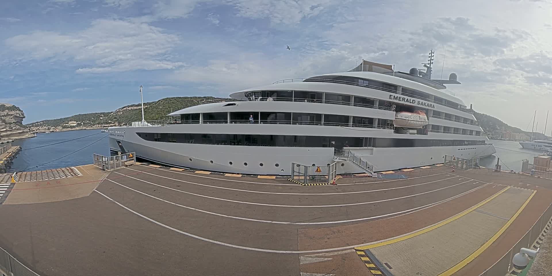 A large white yacht is docked at a port on a partly cloudy day.