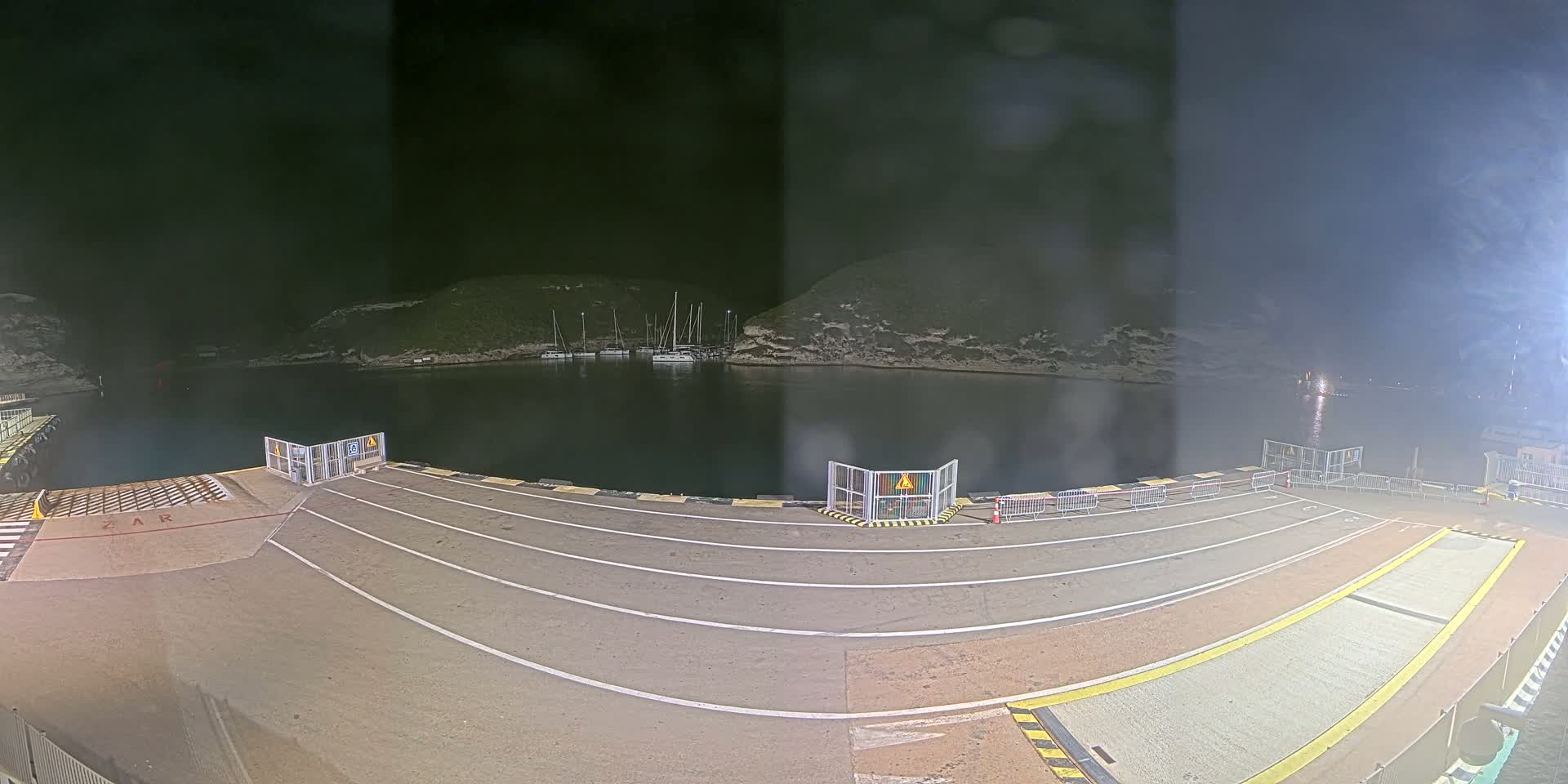 A nighttime view of a ferry dock with several boats moored in a calm bay, under a dark sky.