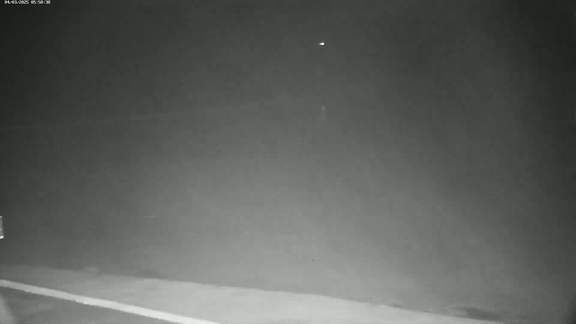 A nighttime, low-light image shows a mostly empty, dark gray scene with a faint white line at the bottom, possibly a road marking.