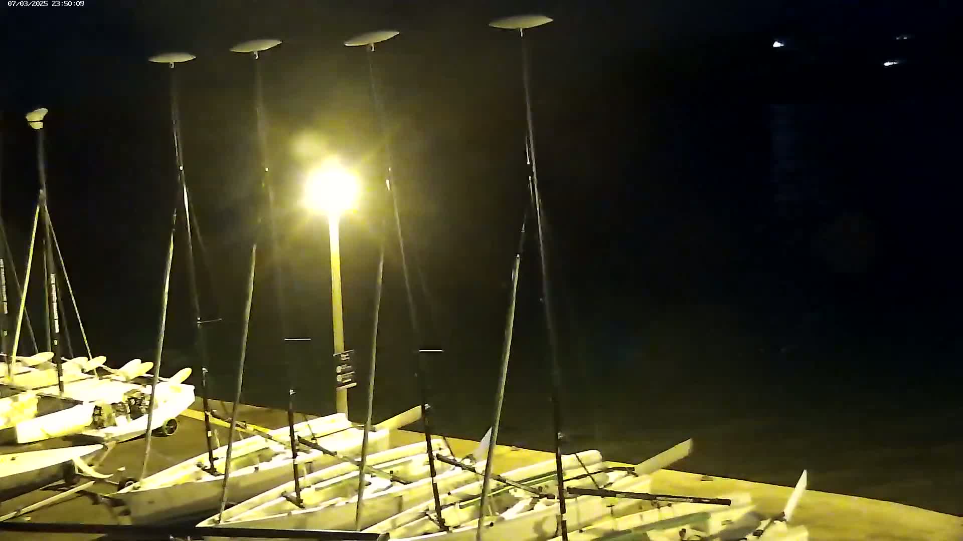 Several small sailboats are docked at night next to a brightly lit dock.