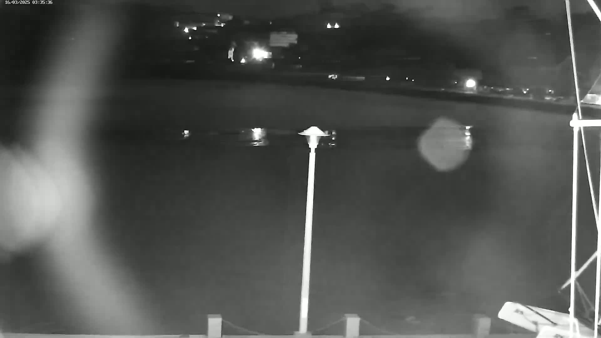 A nighttime, low-light view of a body of water with a single lamppost in the foreground and a dimly lit shoreline in the background.