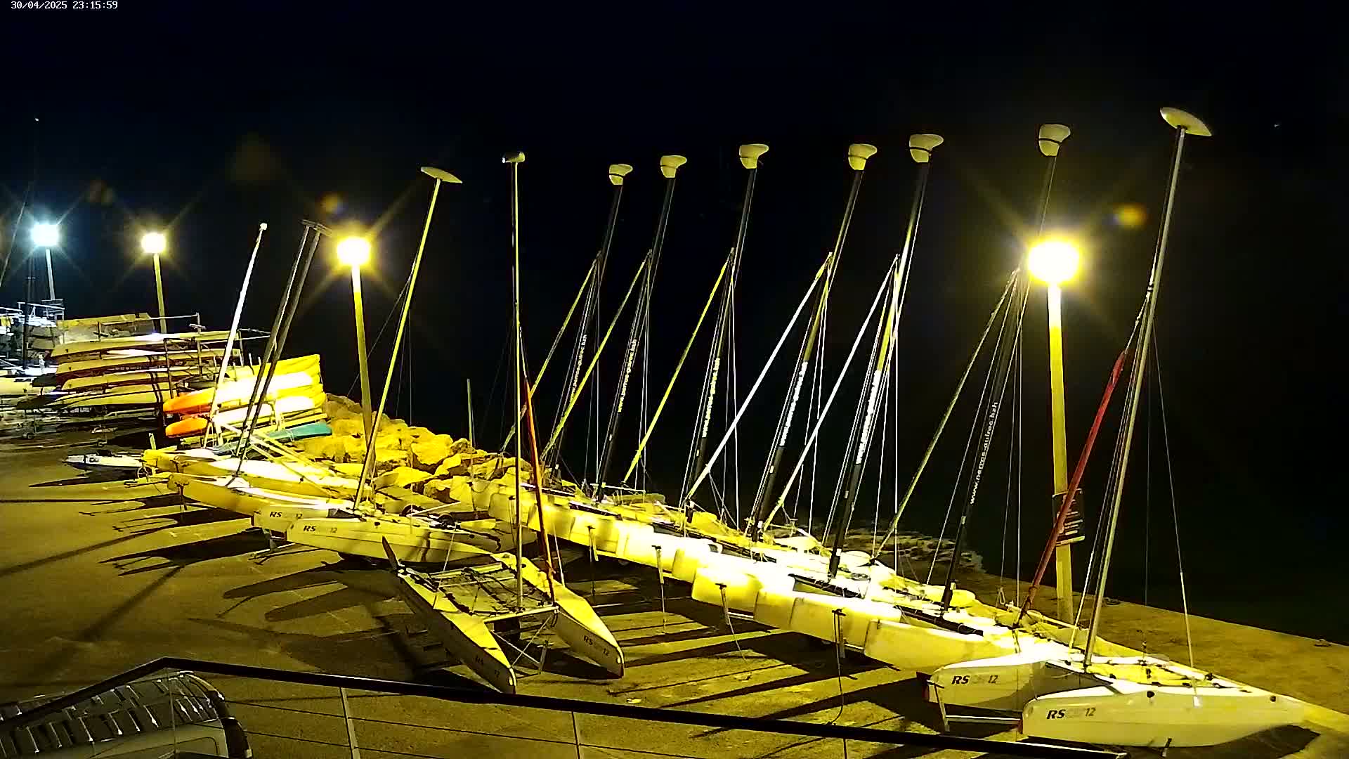 Several sailboats are docked at night under bright artificial lighting.