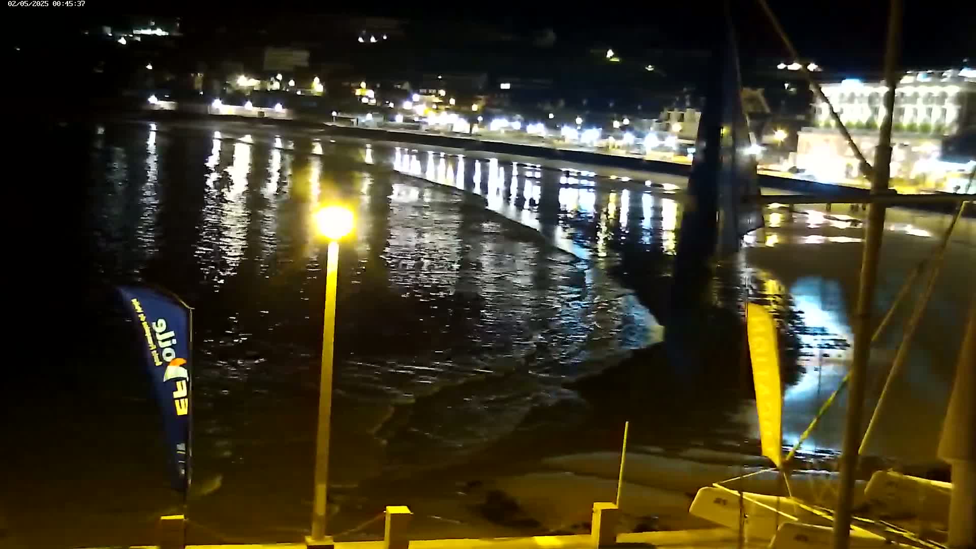 At night, gently lapping waves reflect the lights of a town's waterfront buildings onto the dark water.