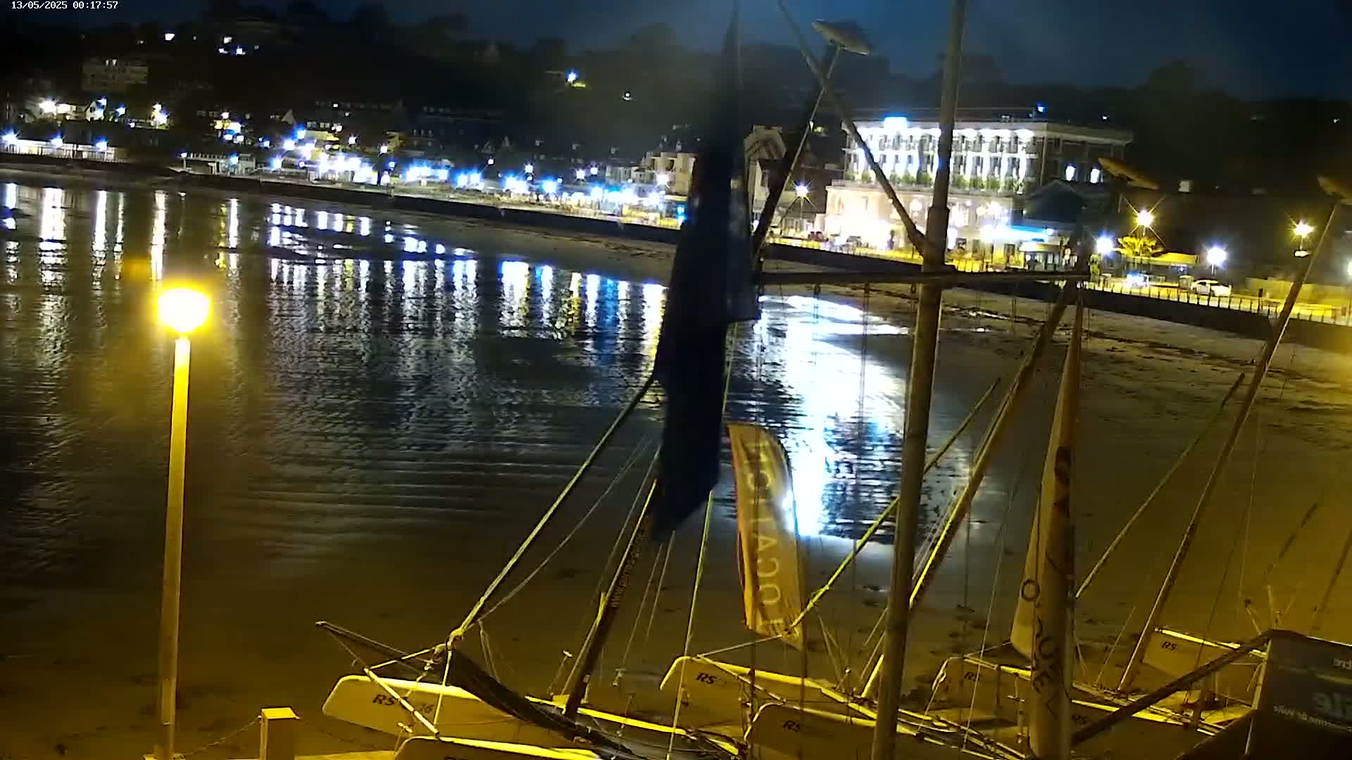 Several sailboats are beached at night near a waterfront town with lights reflecting on the calm water.