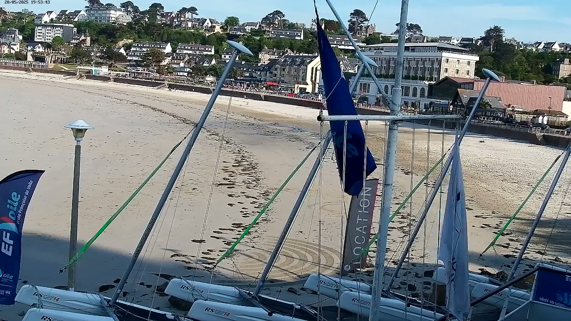 Several sailboats are beached on a sandy shore near a town under a clear, sunny sky.