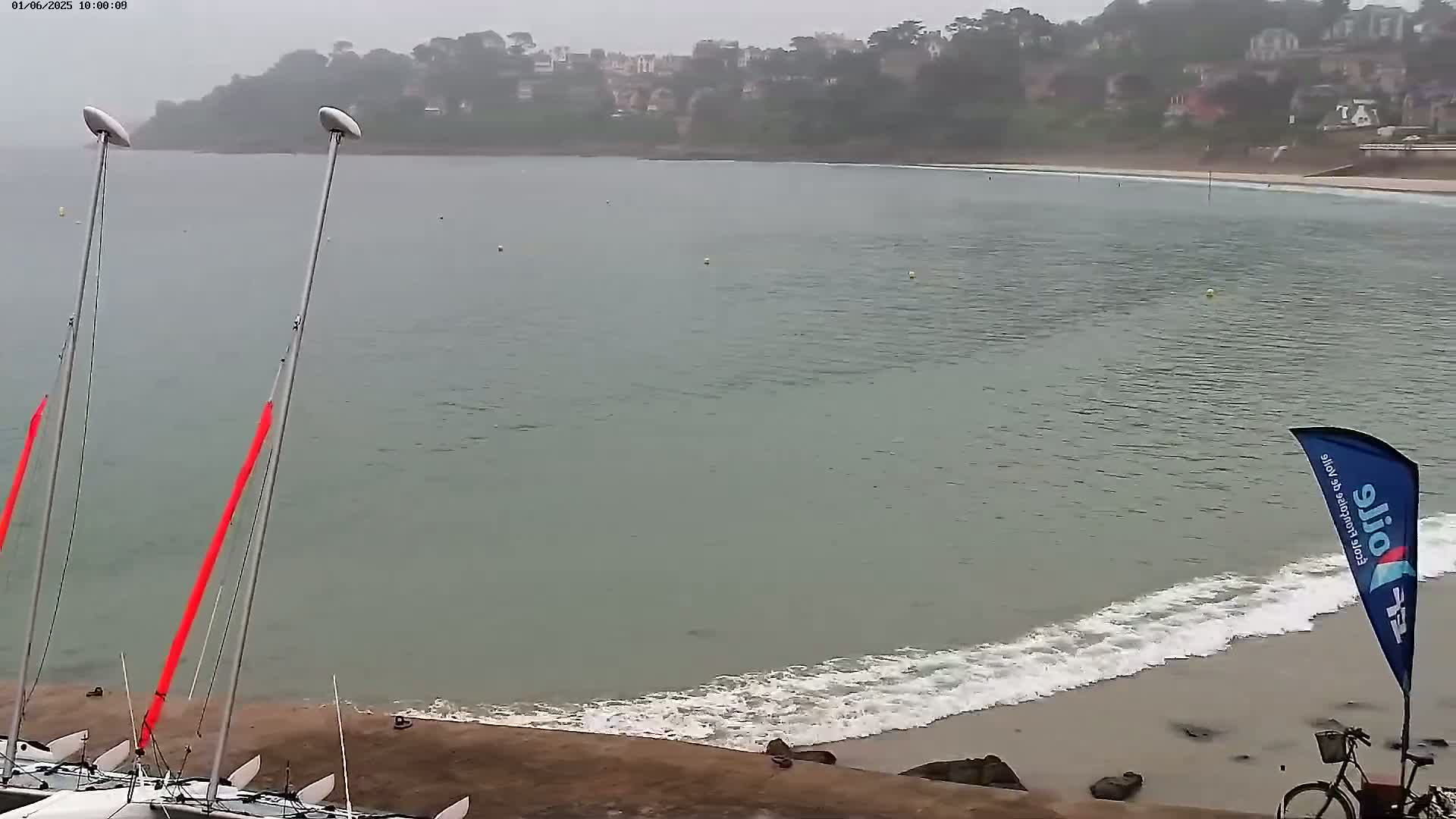 A calm, overcast day at a beach with two sailboats and a bicycle near the shore.