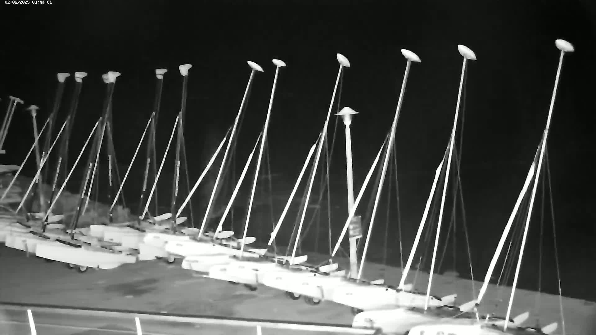 A row of sailboats are docked at night under a dark sky.