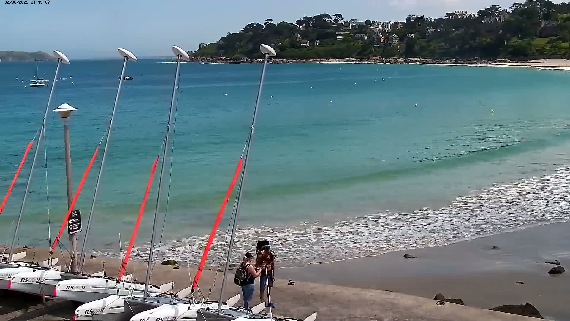 Several small sailboats are moored on a sandy beach next to a calm, turquoise ocean under a sunny sky.