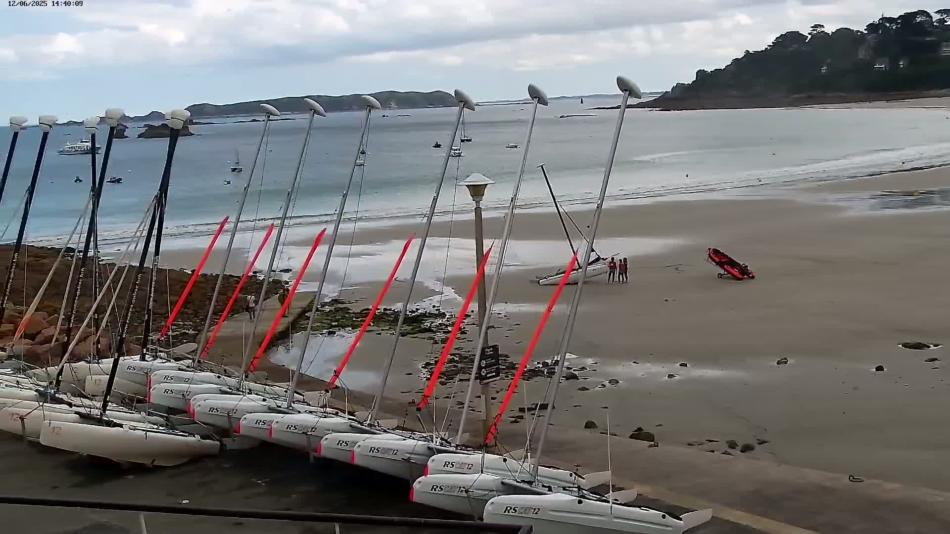Several sailboats are beached on a sandy shore under an overcast sky, with one capsized sailboat and a small red boat nearby.