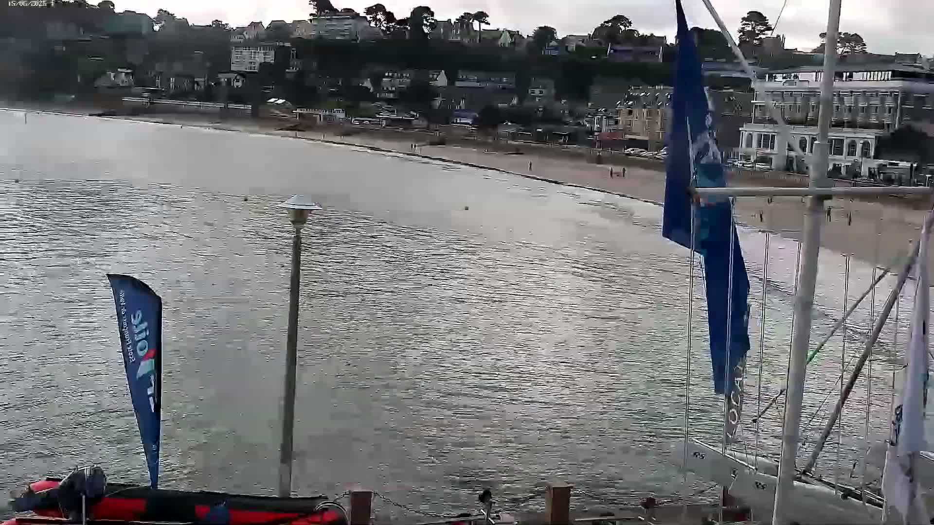 A mostly cloudy day shows a calm body of water with a sandy beach and buildings along the shoreline.