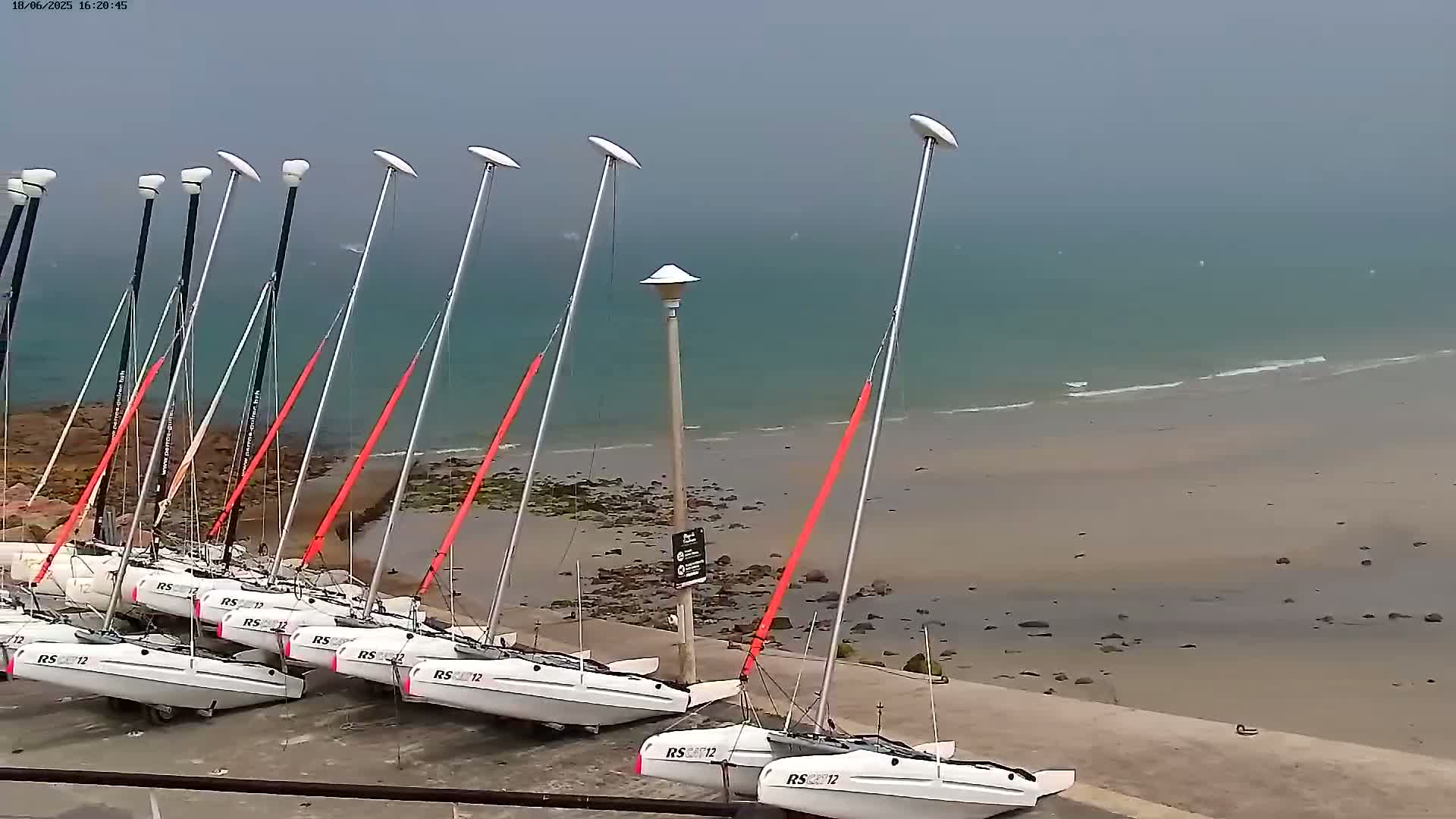 Several small white sailboats are beached on a sandy shore next to a rocky outcrop under an overcast sky.