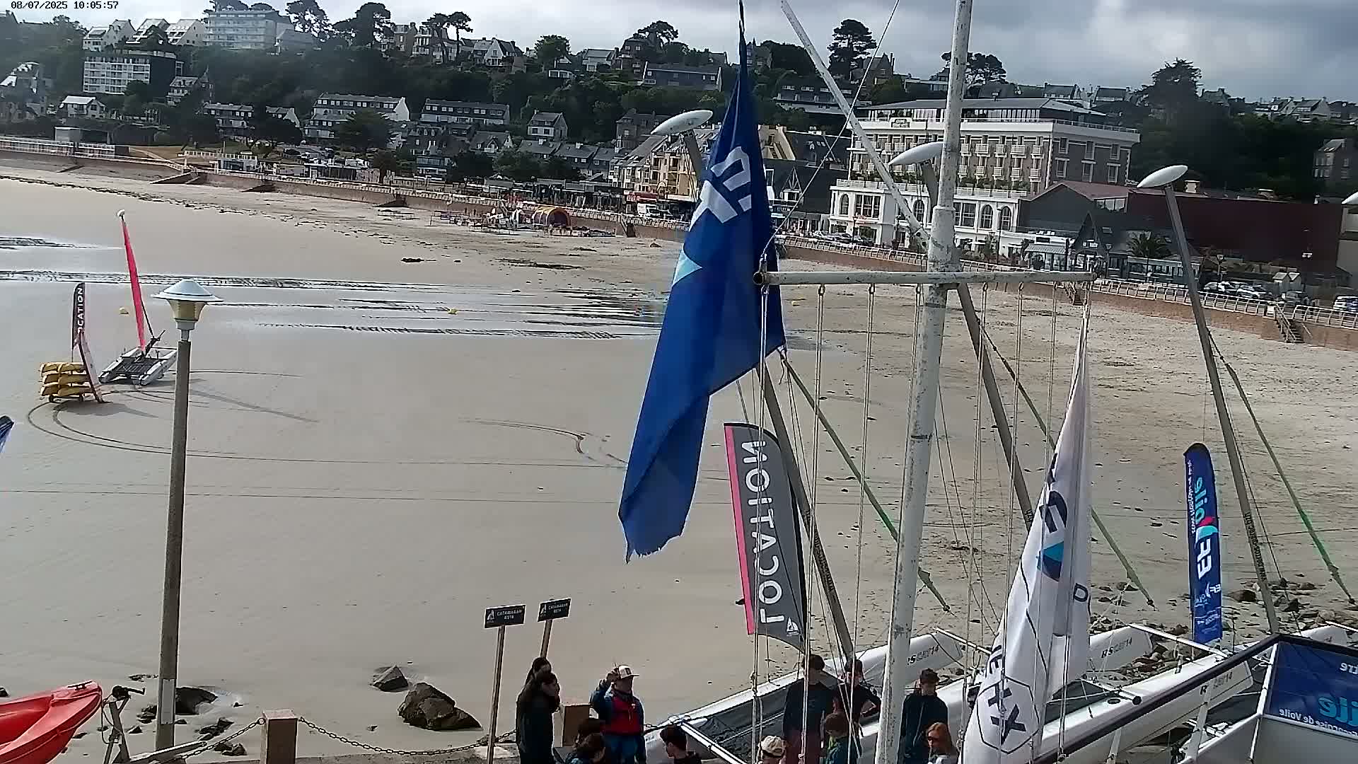 A sandy beach with several sailboats and people gathered near them under overcast skies.