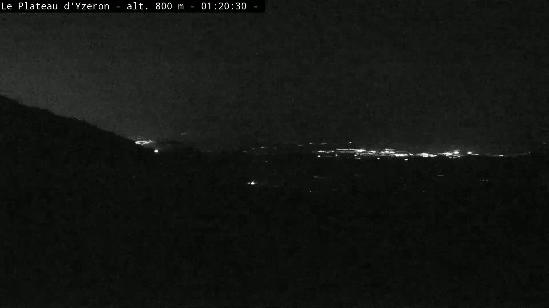 A nighttime, low-light view shows a distant cityscape illuminated with faint lights below a dark, possibly cloudy sky.