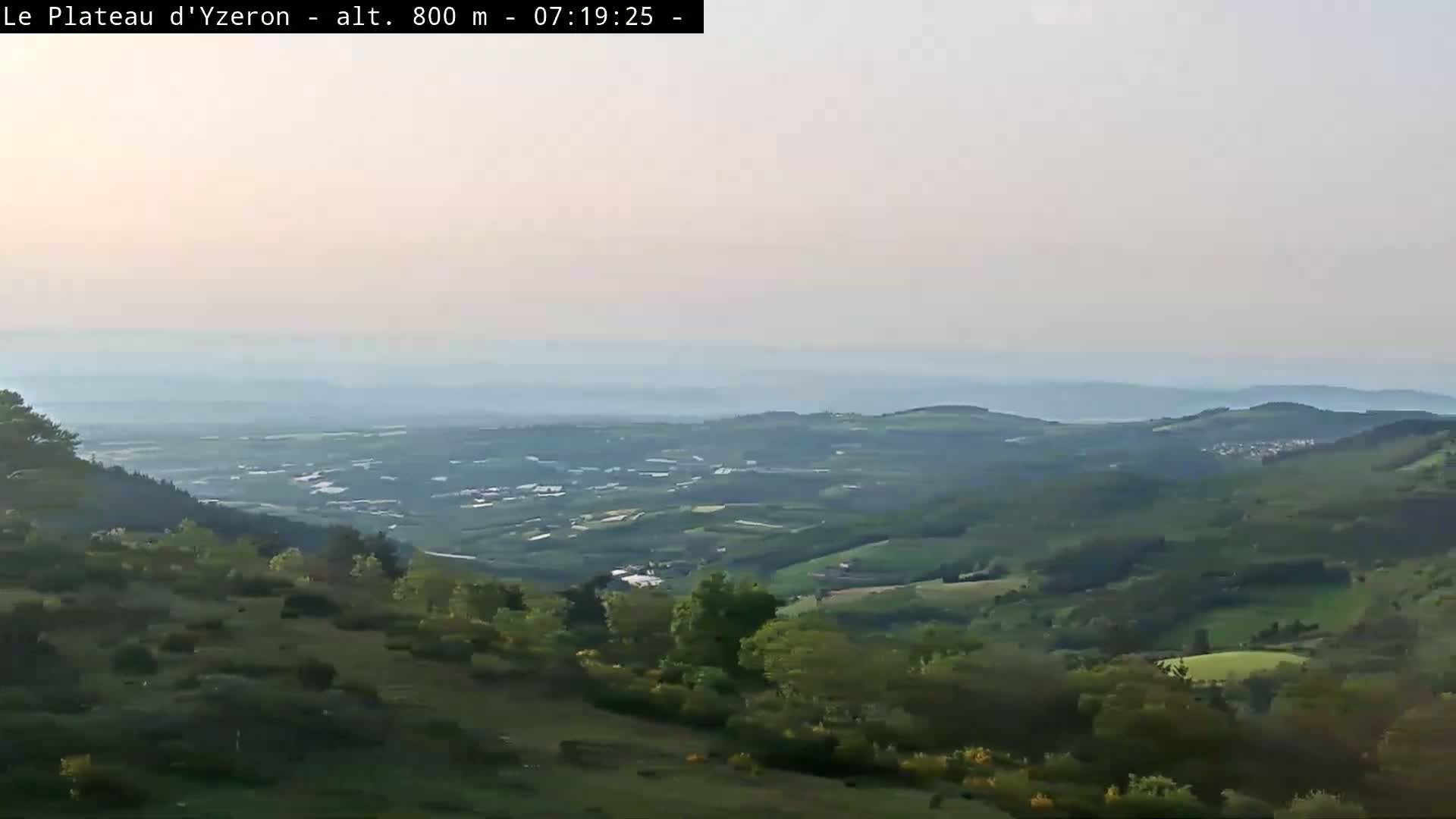 A hazy, expansive view of rolling green hills and valleys extends to a distant horizon under a pale sky.