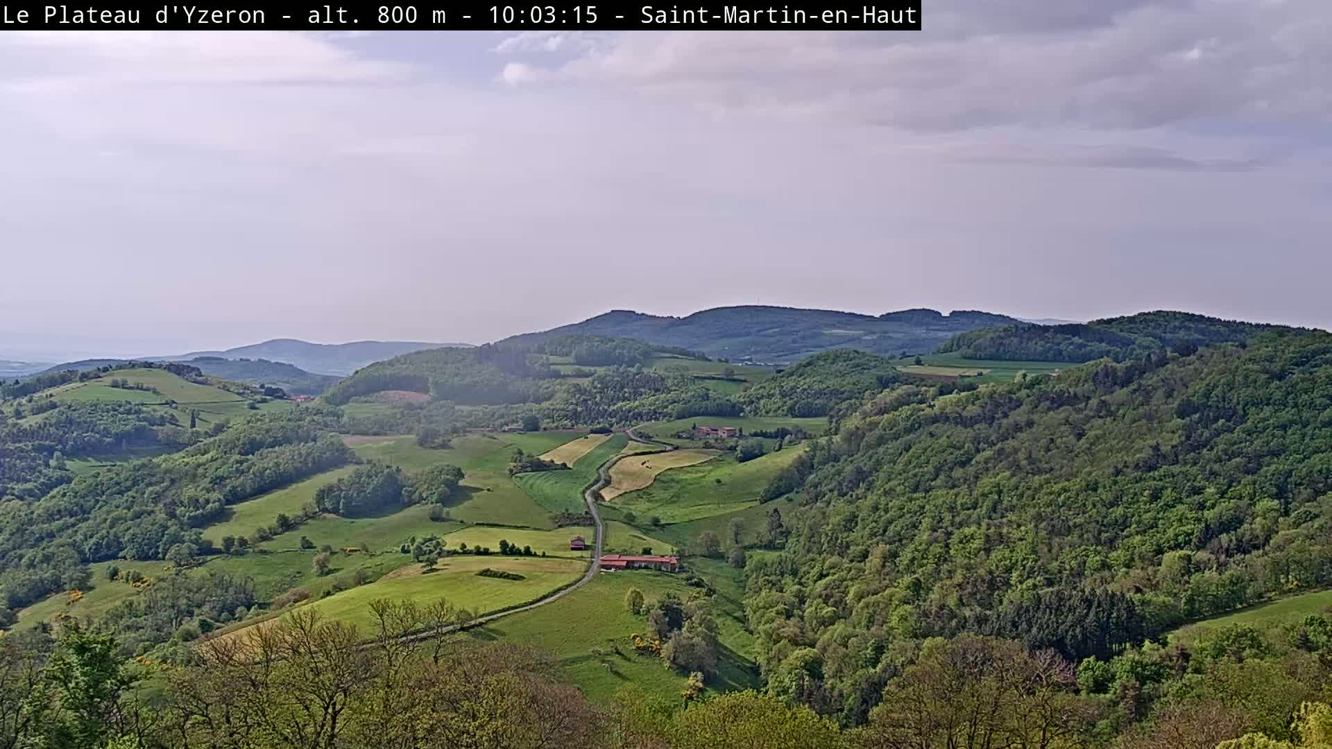 A sprawling landscape of rolling green hills and lush forests under a mostly cloudy sky.