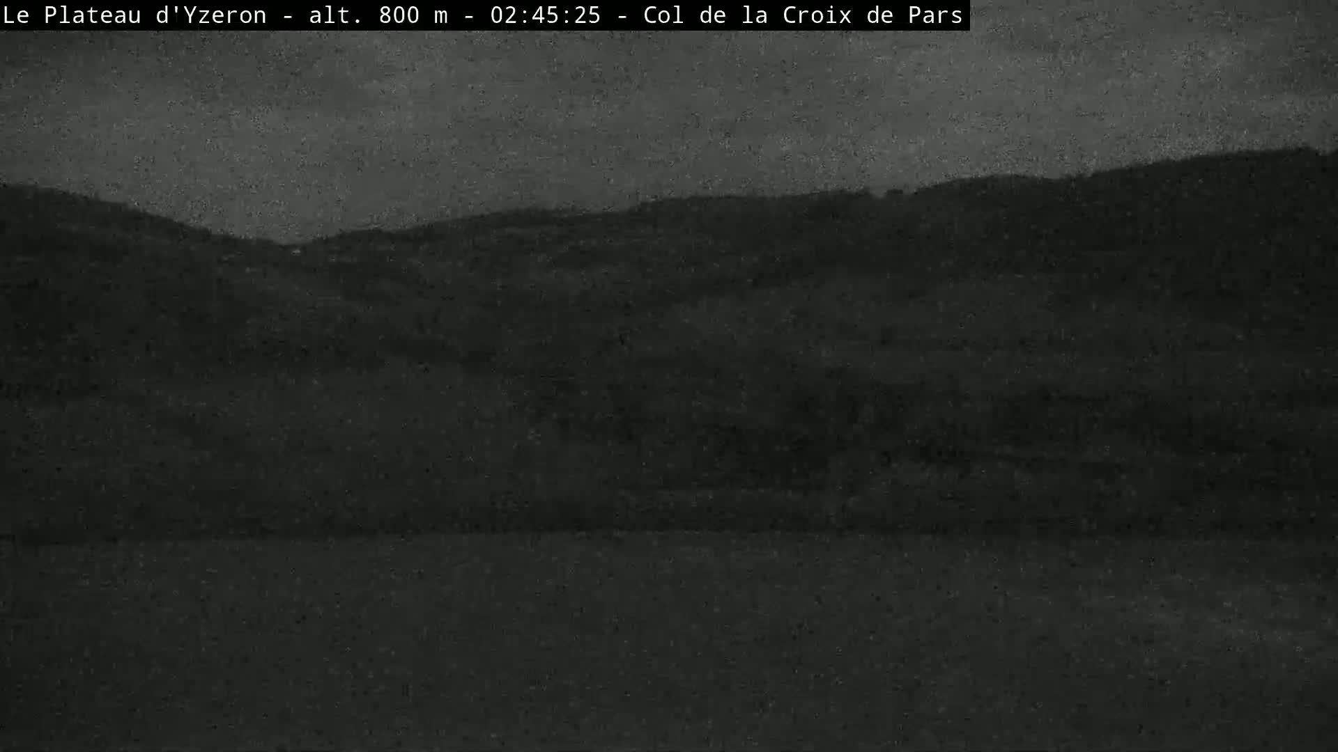 A dark, nighttime view of a hilly landscape under a cloudy sky.