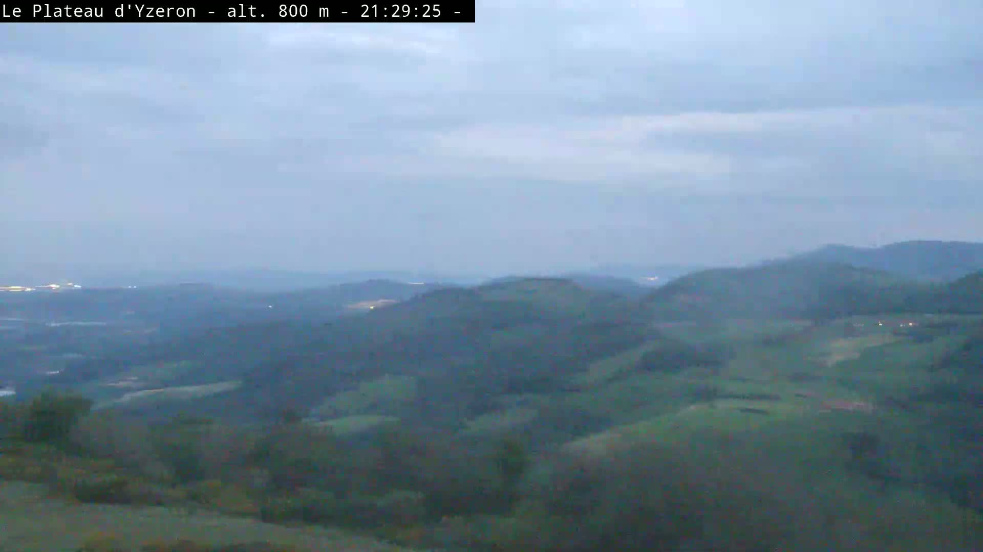 A view of rolling green hills under a hazy, overcast sky at twilight.