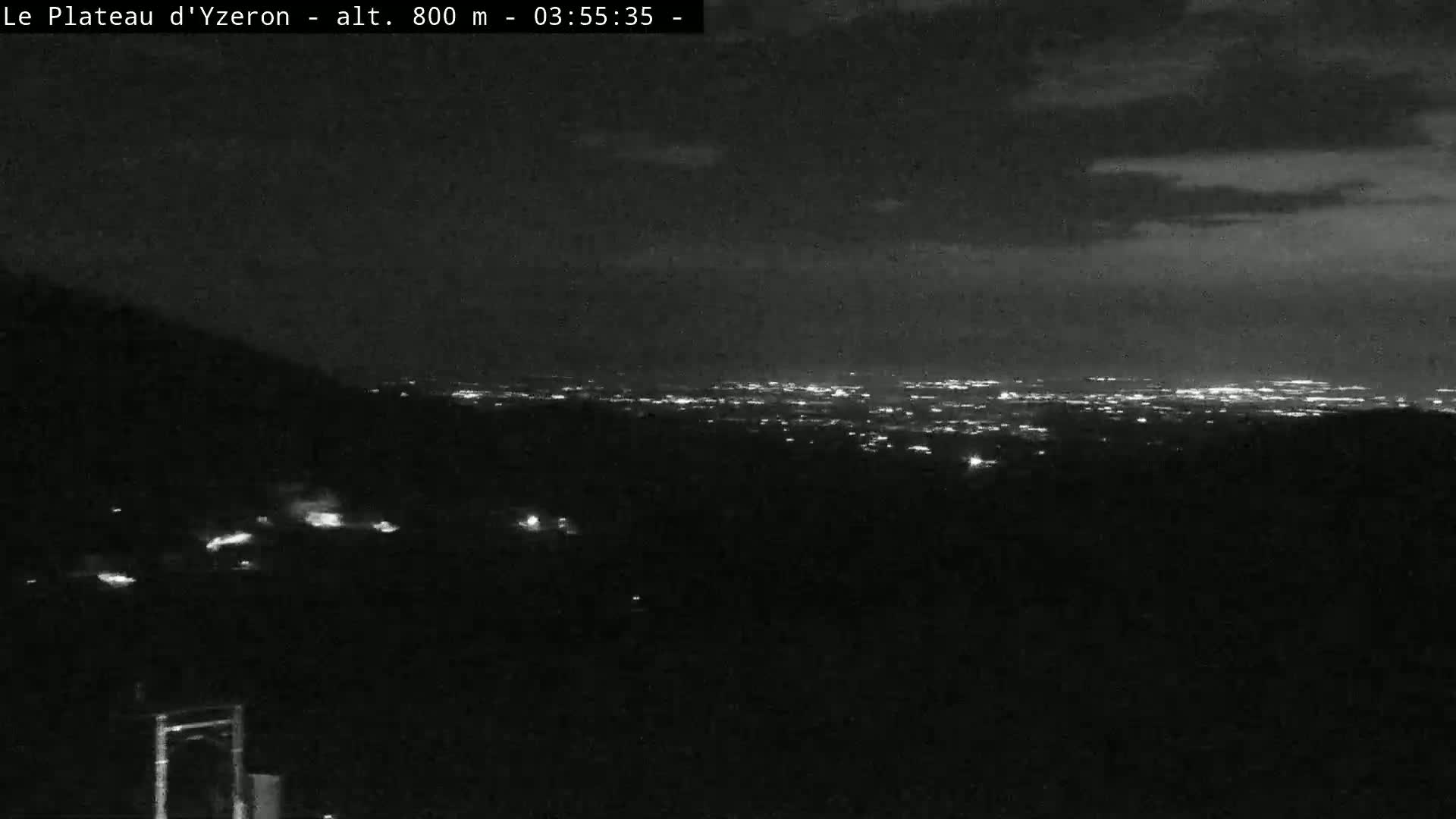 A nighttime view shows a distant city glowing with lights under a partly cloudy sky.