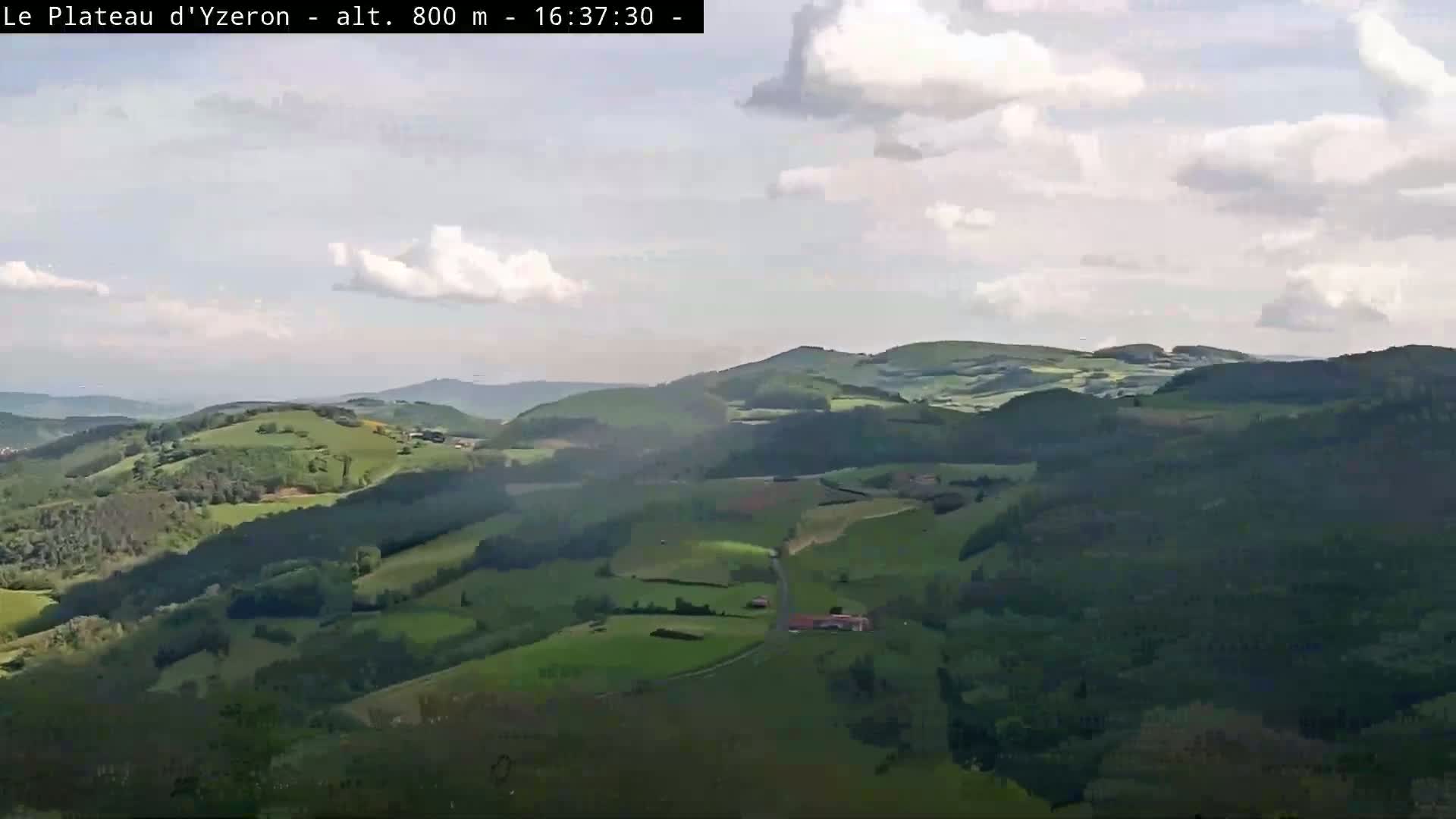 A partly cloudy sky overlooks a vast expanse of rolling green hills and valleys.