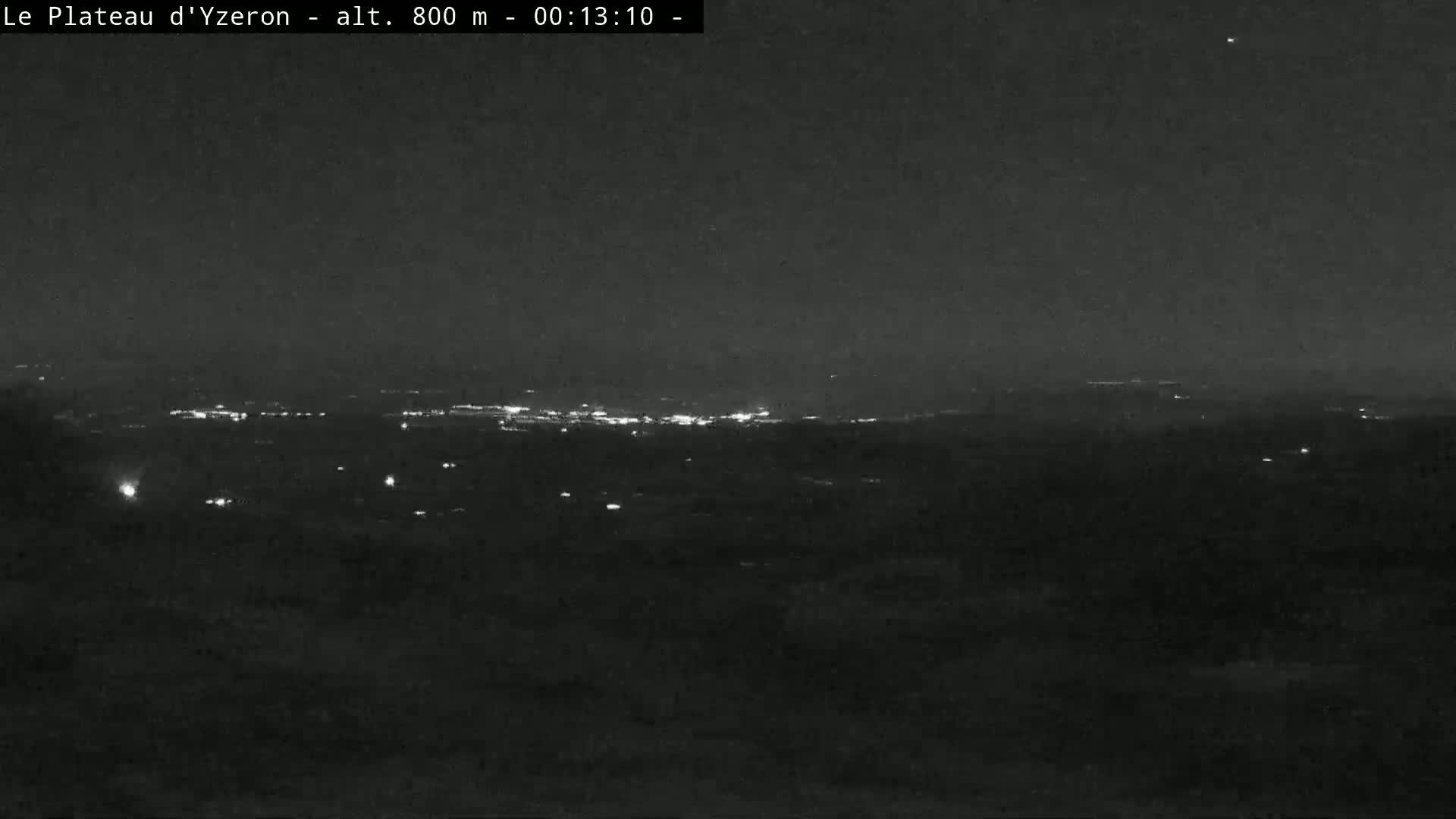 A nighttime, long-range view shows a dark landscape with a distant line of city lights under a clear, dark sky.