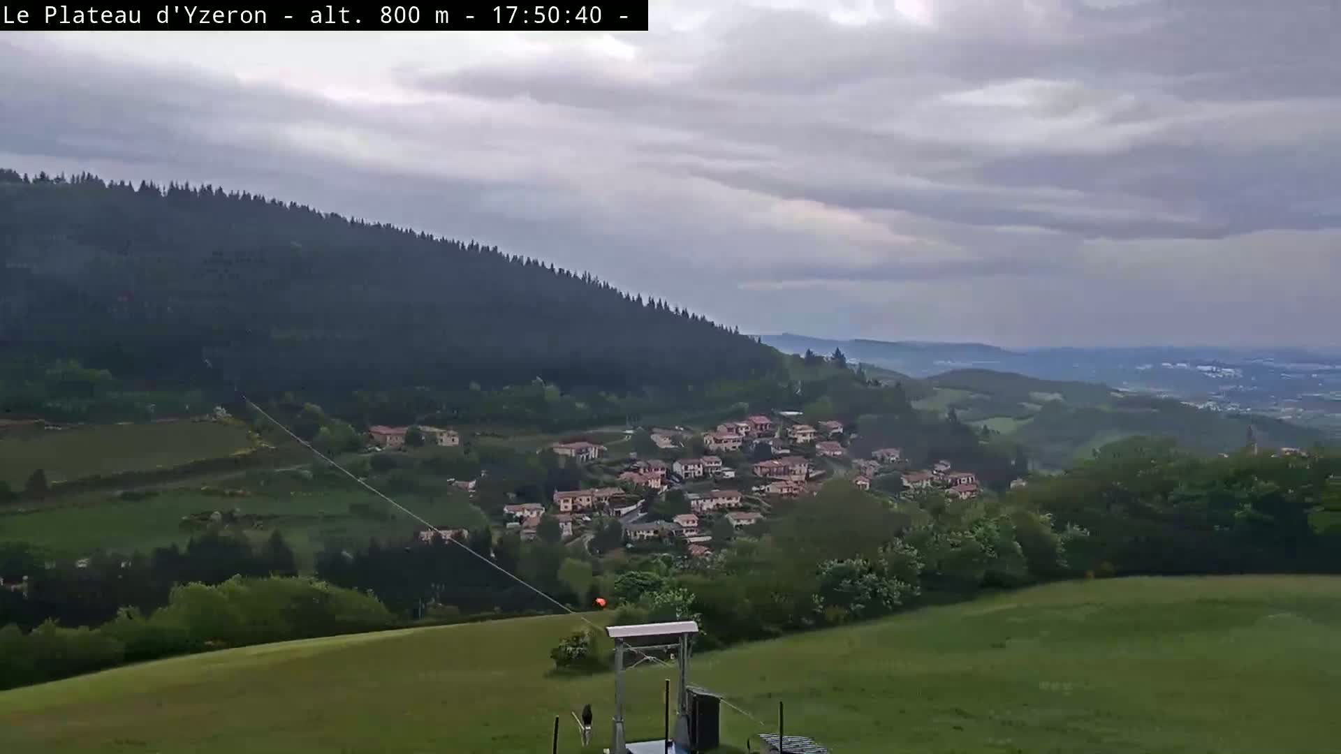 A small village nestled in a valley is viewed from a hillside under an overcast sky.