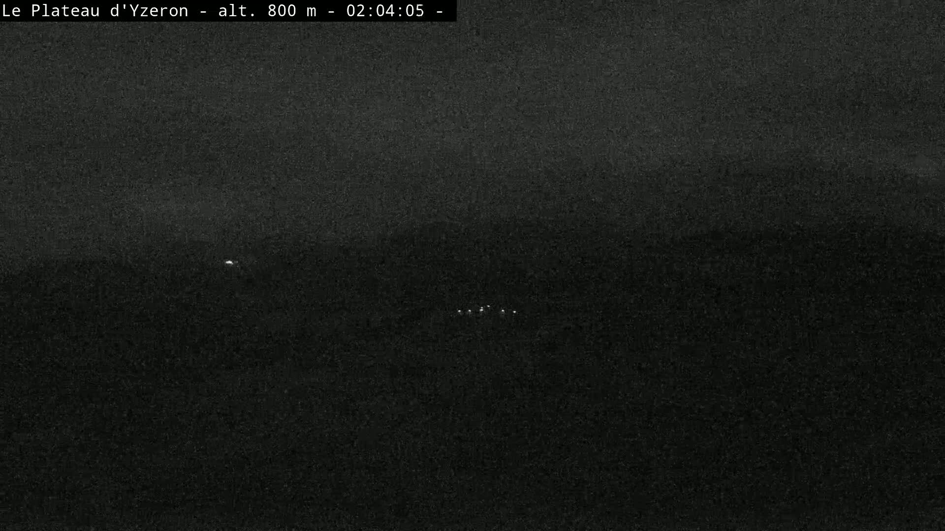 A dark, nighttime landscape with a few small, distant lights visible.