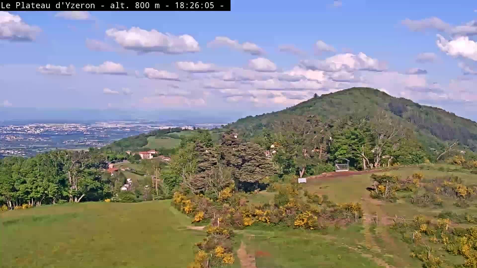 A panoramic view shows a verdant hillside with a distant city under a partly cloudy sky.