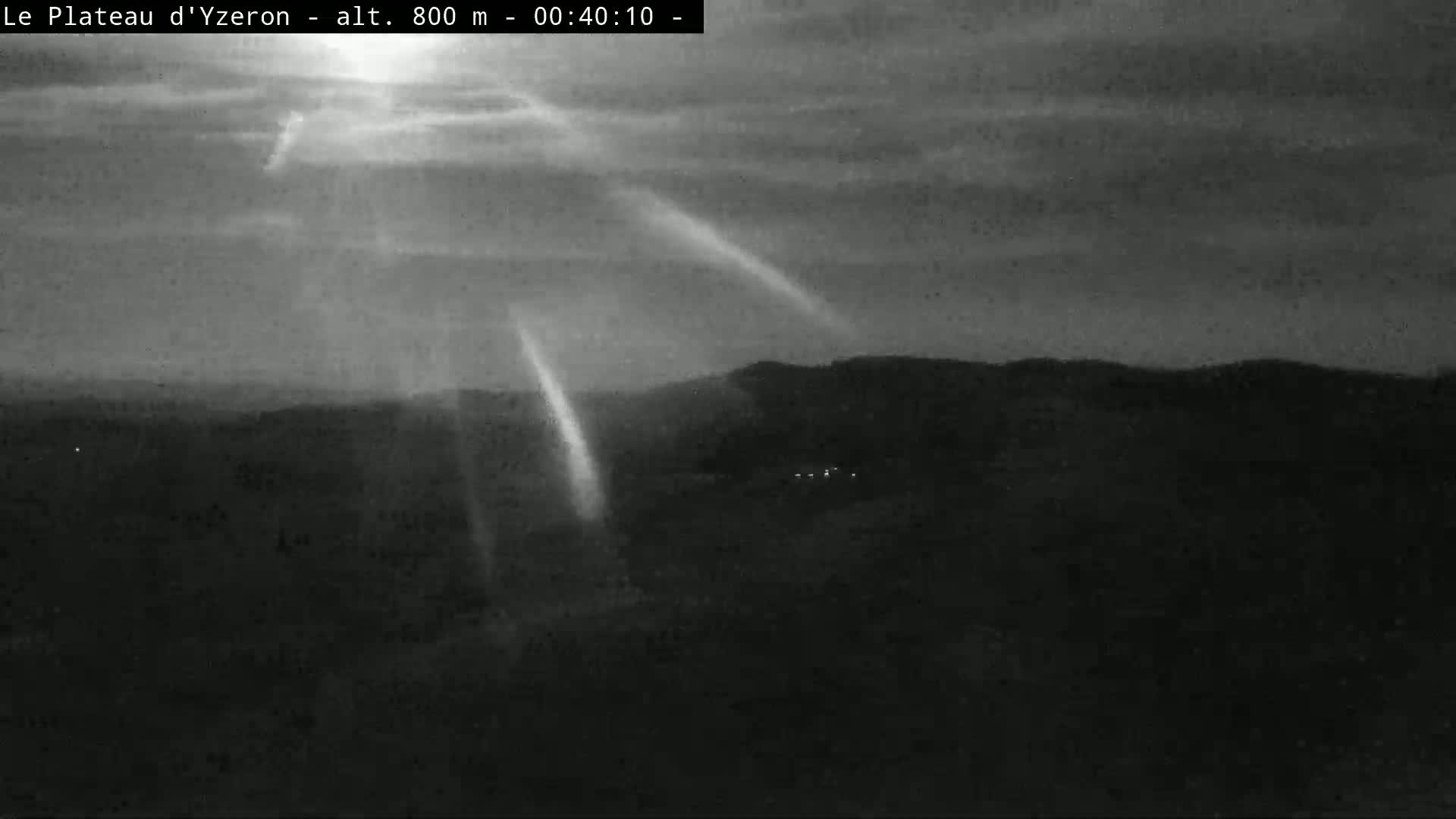 Crepuscular rays illuminate a dark, hilly landscape under a cloudy, twilight sky.