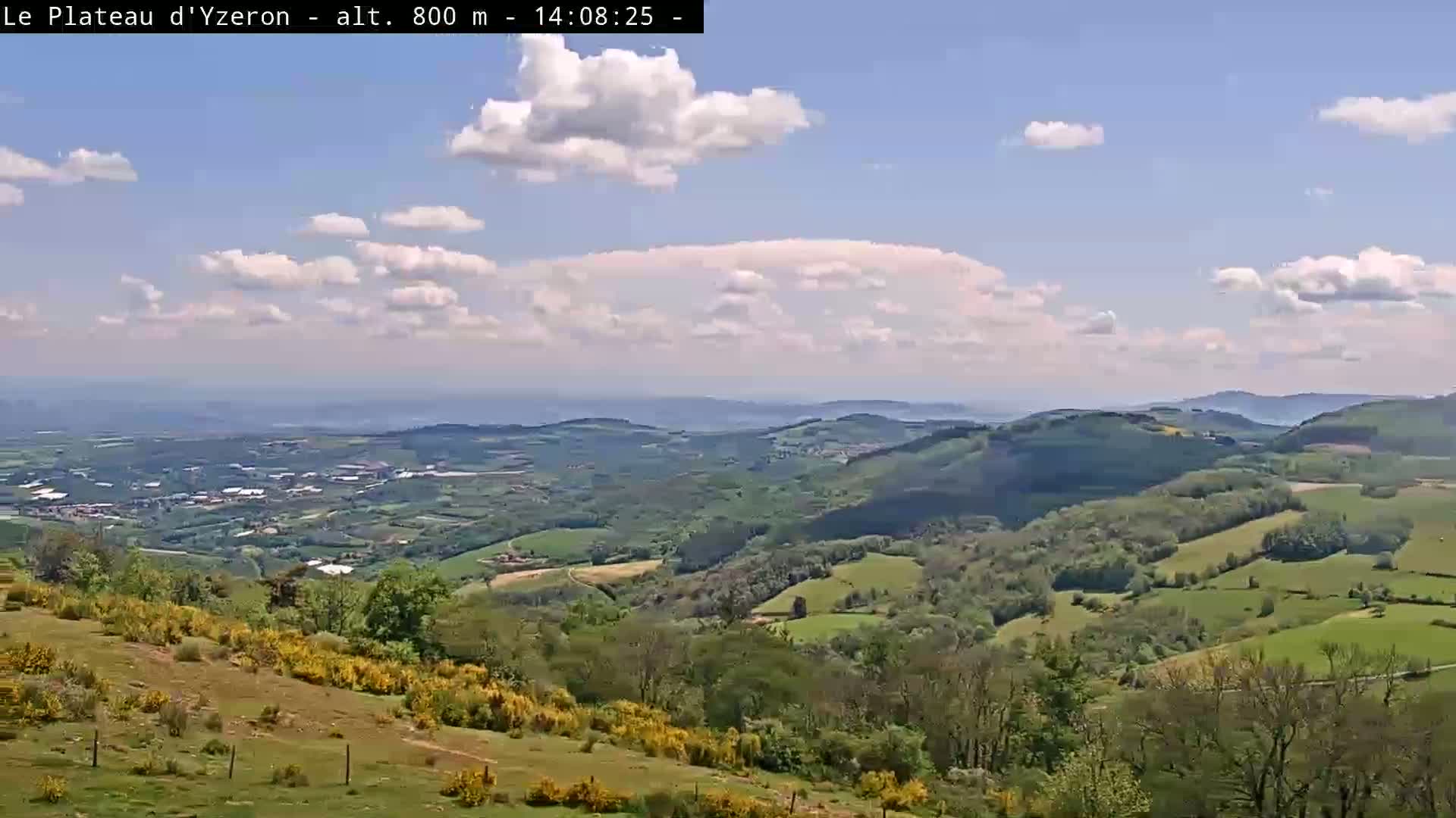 A partly cloudy day reveals a sweeping vista of rolling green hills and valleys, extending to a distant horizon.