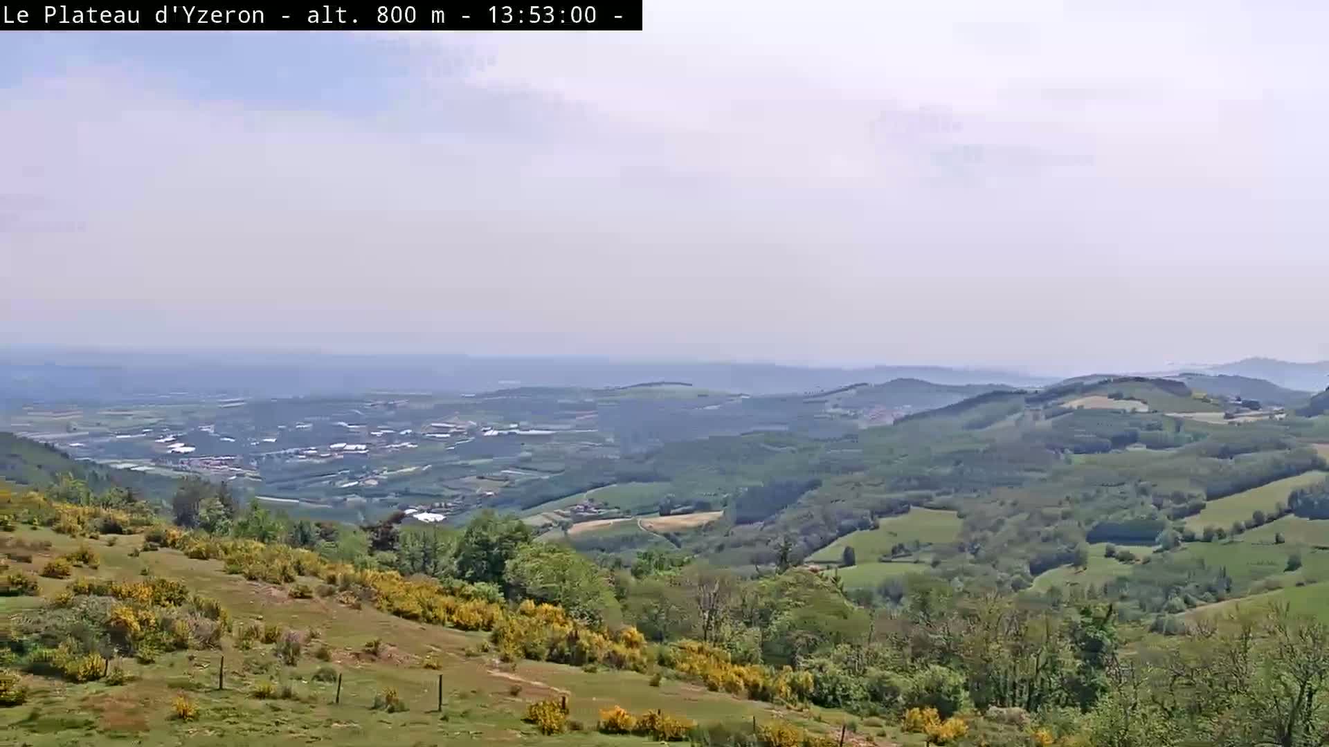 A hazy, expansive view of rolling green hills and valleys stretches to a distant horizon under a mostly clear sky.