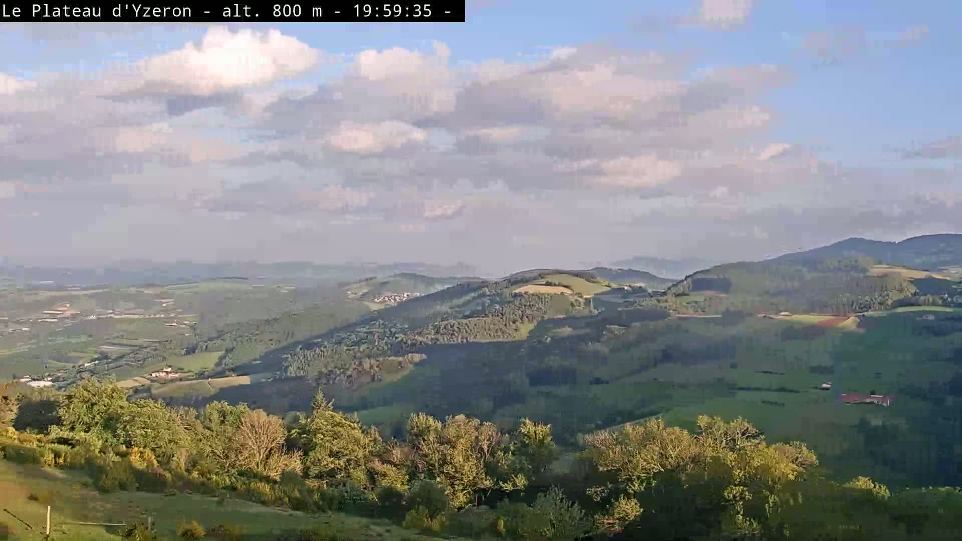 A partly cloudy sky overlooks a vast, rolling landscape of green hills and valleys.