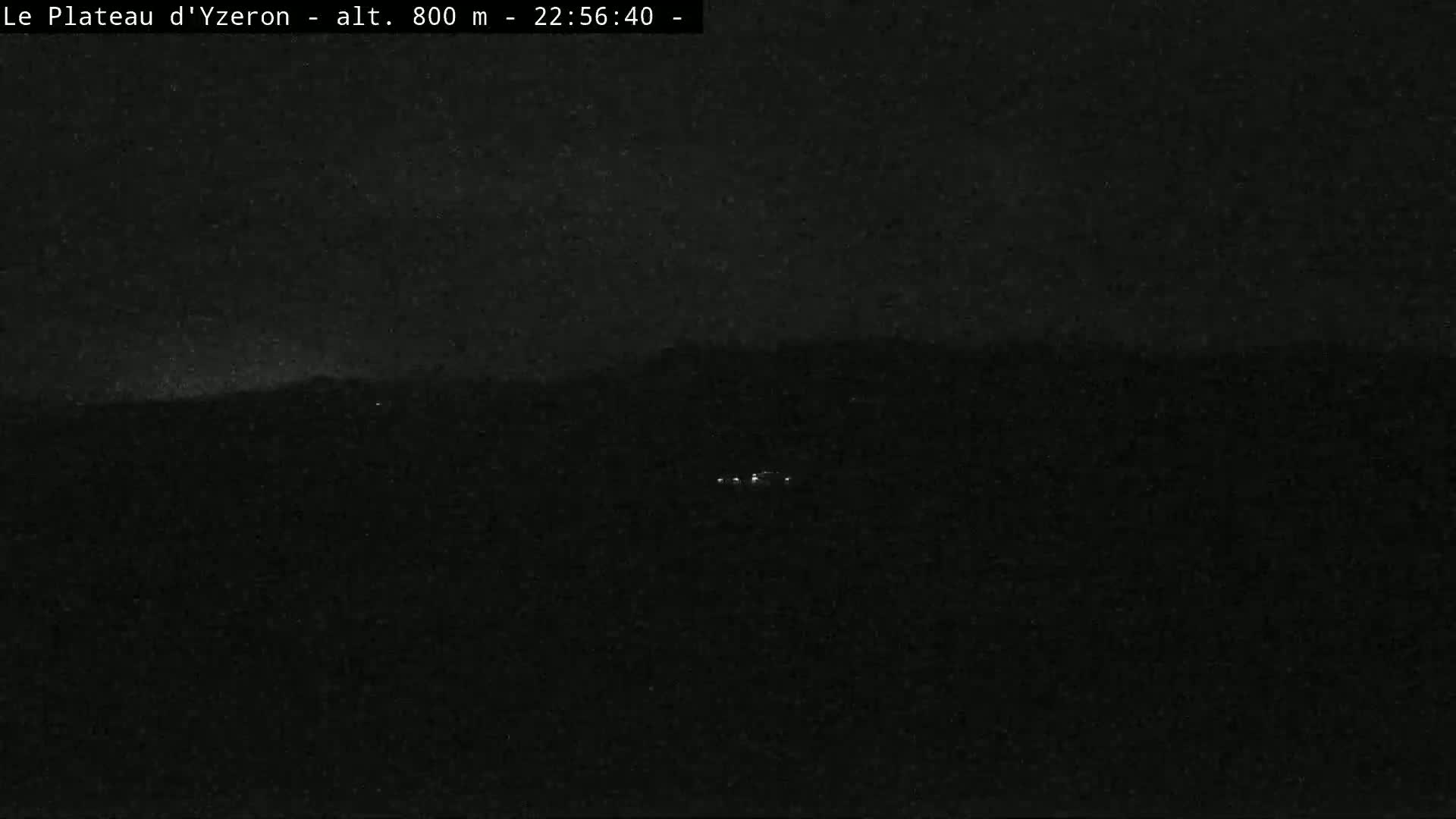 A dark, nighttime landscape is visible, showing a few faint lights in the distance under a mostly clear sky.