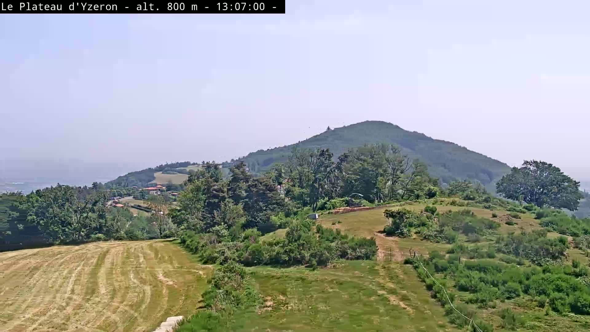 A hazy, sunny day reveals a verdant landscape with rolling hills, patches of mowed grass, and a distant mountain range.