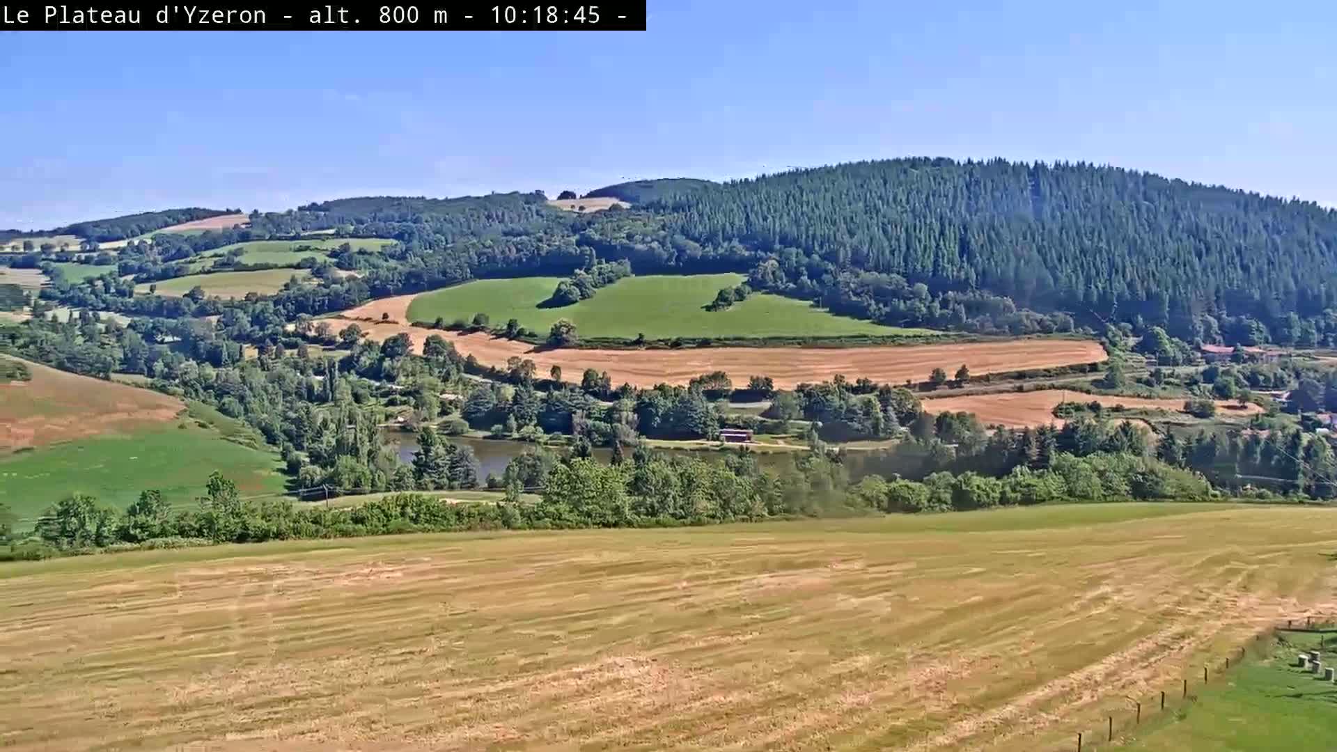 A panoramic view shows rolling hills of farmland and forest under a clear blue sky.