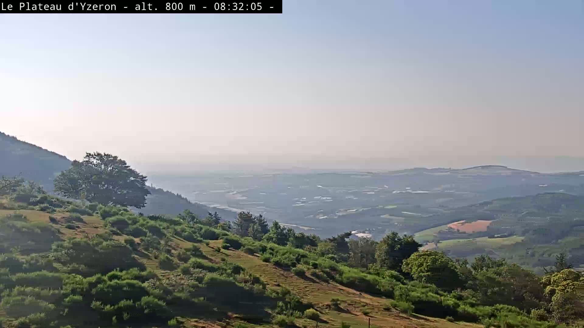 A hazy, sunny view from a hilltop shows a vast expanse of rolling hills and valleys stretching to a distant horizon.