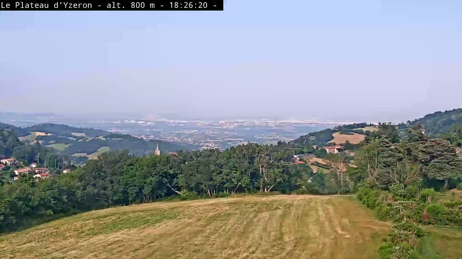 A hazy, sunny view from a hilltop shows a vast expanse of rolling green hills and a distant city spread out below.