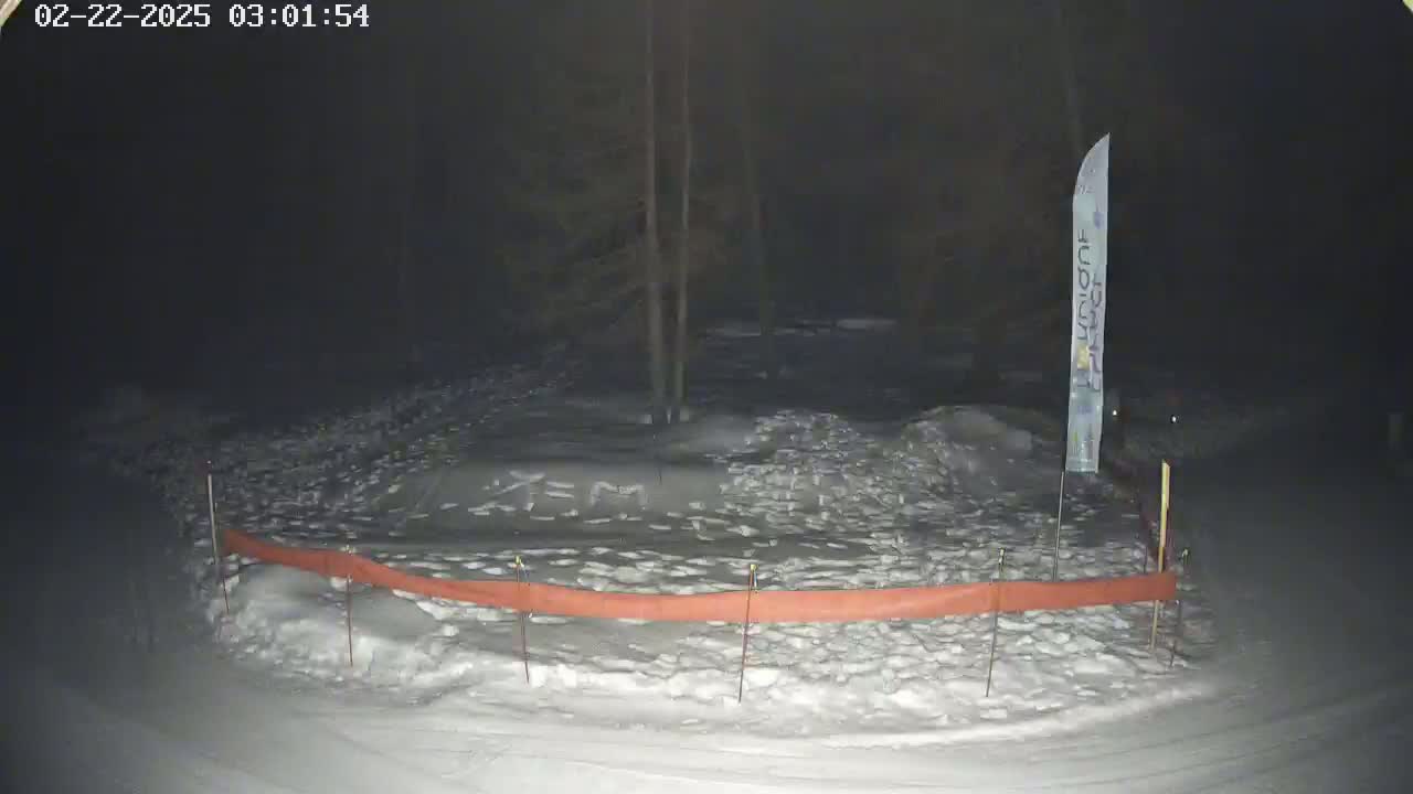 A snow-covered area at night, partially enclosed by an orange barrier, is illuminated by dim light.