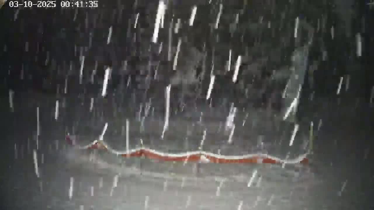 A long, low, reddish-orange object lies on the ground in heavy snowfall at night.