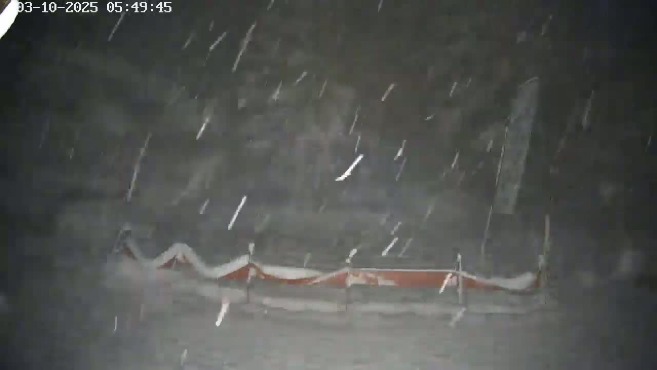 Snow is falling heavily on a low, reddish-brown structure partially covered in snow.