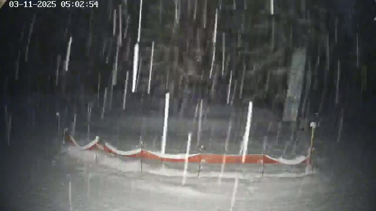 A low-lying, red and white structure is partially visible in the snow during a heavy nighttime snowfall.
