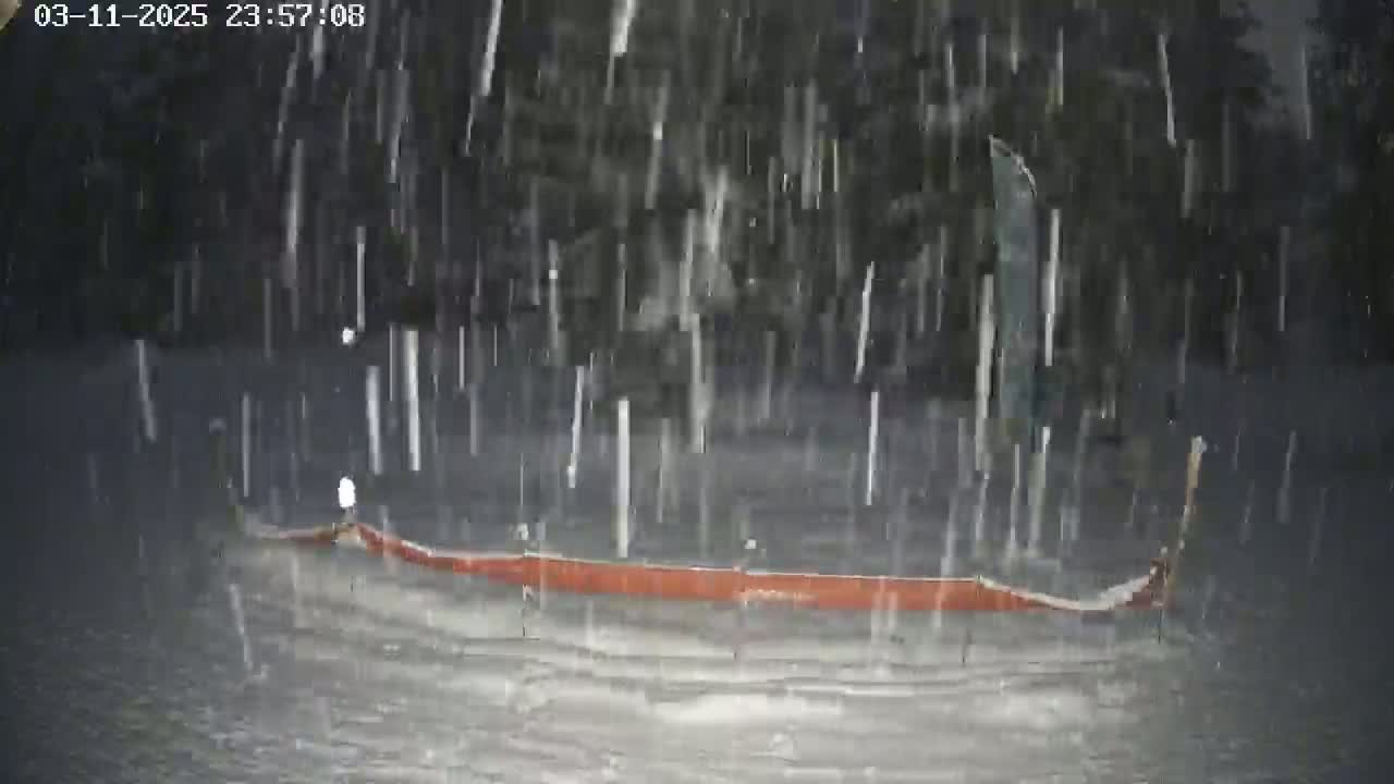 A long, low, orange object sits in the snow during a heavy snowfall at night.