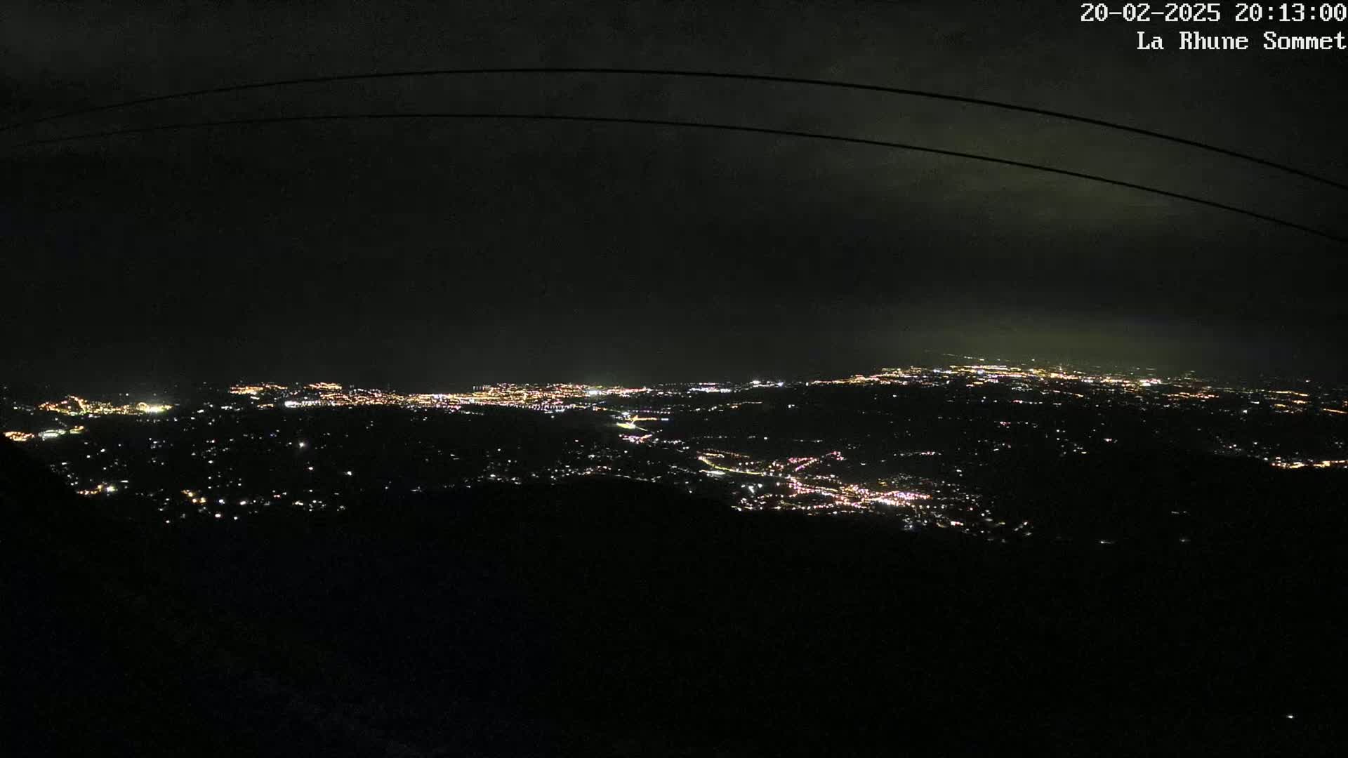 A nighttime, high-angle view shows a sprawling city illuminated by scattered lights against a dark, cloudy sky.