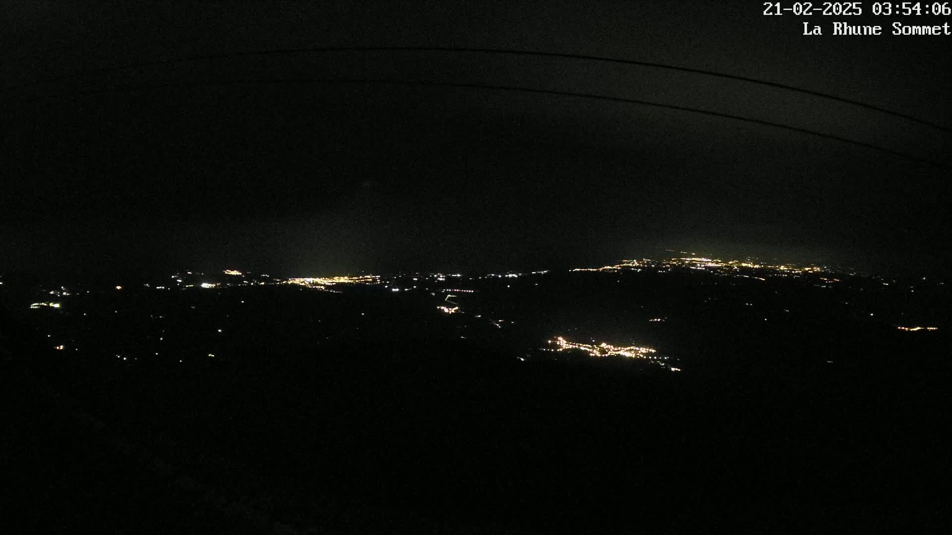 A nighttime view shows distant city lights spread across a dark landscape under a clear, dark sky.