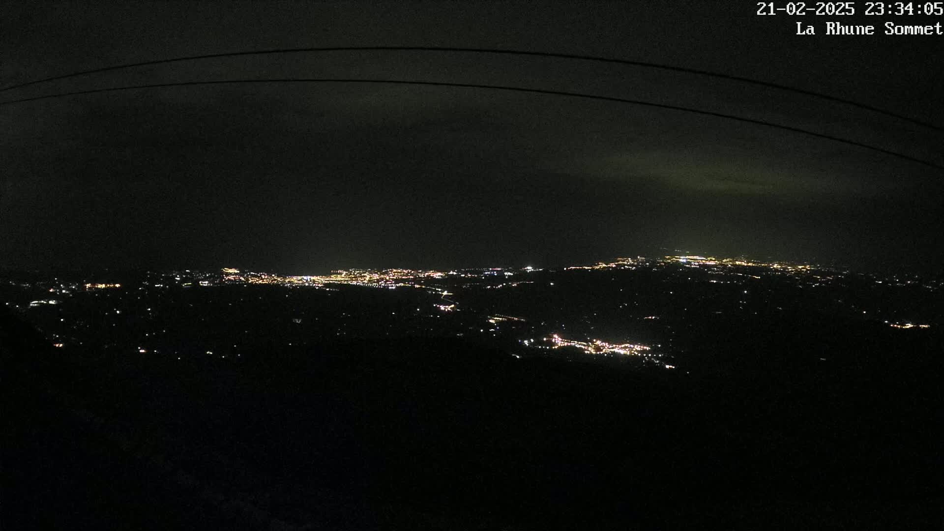 A nighttime view shows a sprawling city illuminated by many small lights, visible from a high vantage point under a dark, cloudy sky.