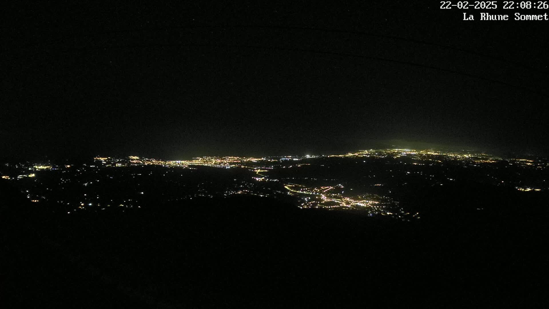 A nighttime, high-angle view shows a sprawling city illuminated by numerous lights, extending into the distance under a clear, dark sky.