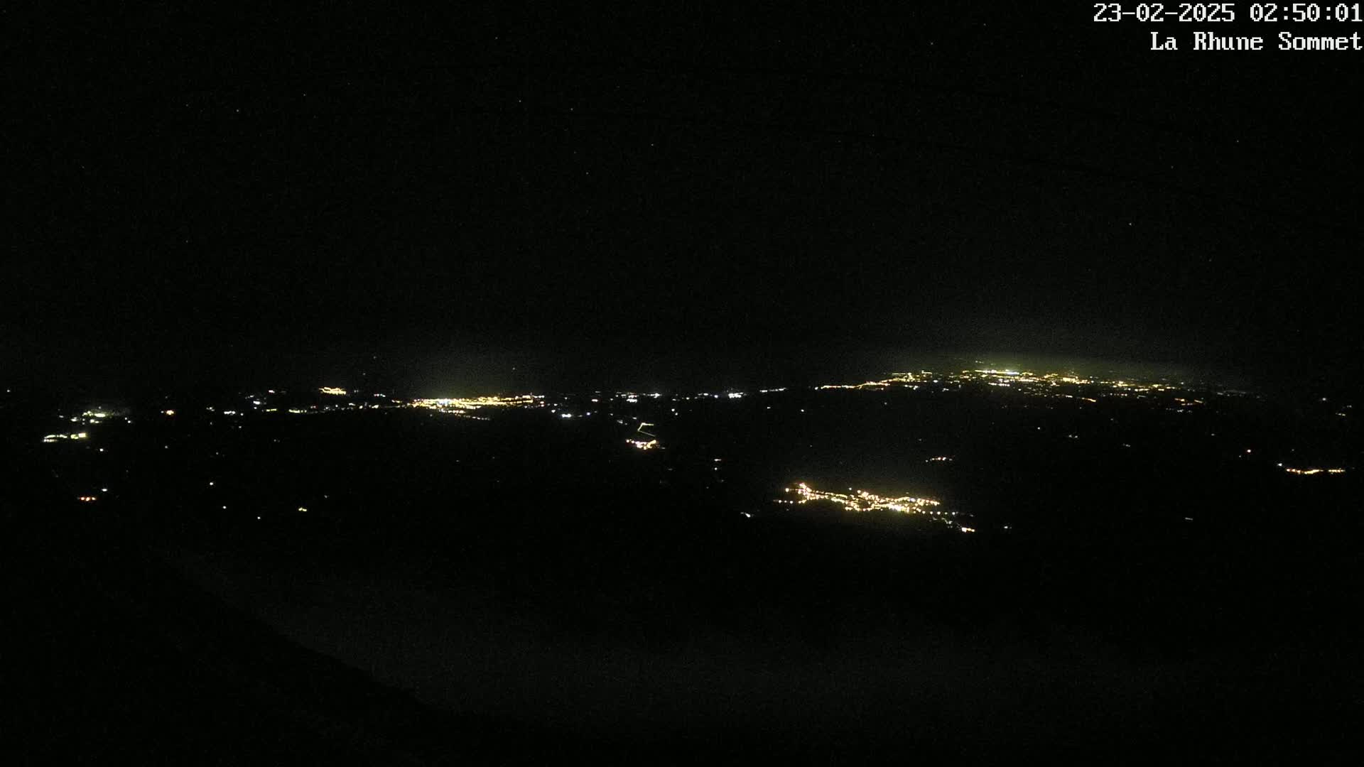 A nighttime long shot reveals a sprawling landscape dotted with the faint lights of distant towns and cities under a clear, dark sky.