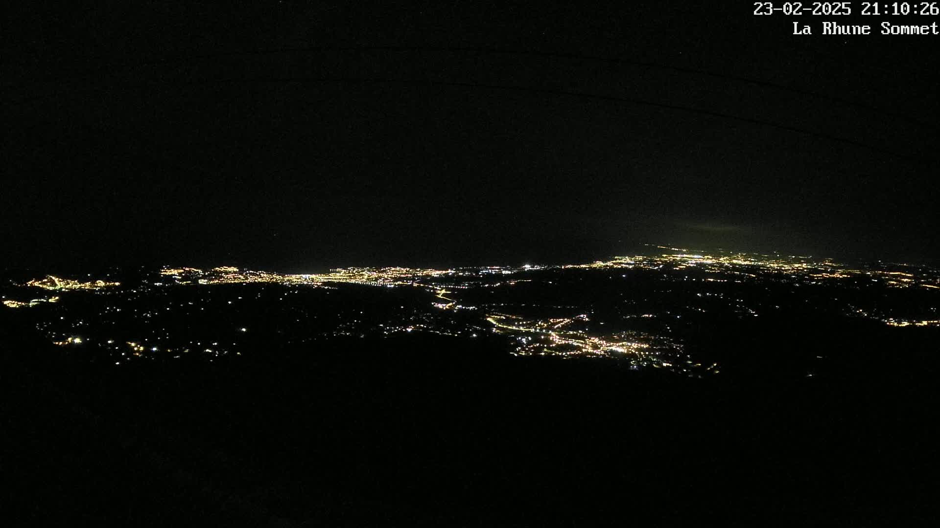 A nighttime, high-angle view of a sprawling city illuminated by countless lights spread across a dark landscape.