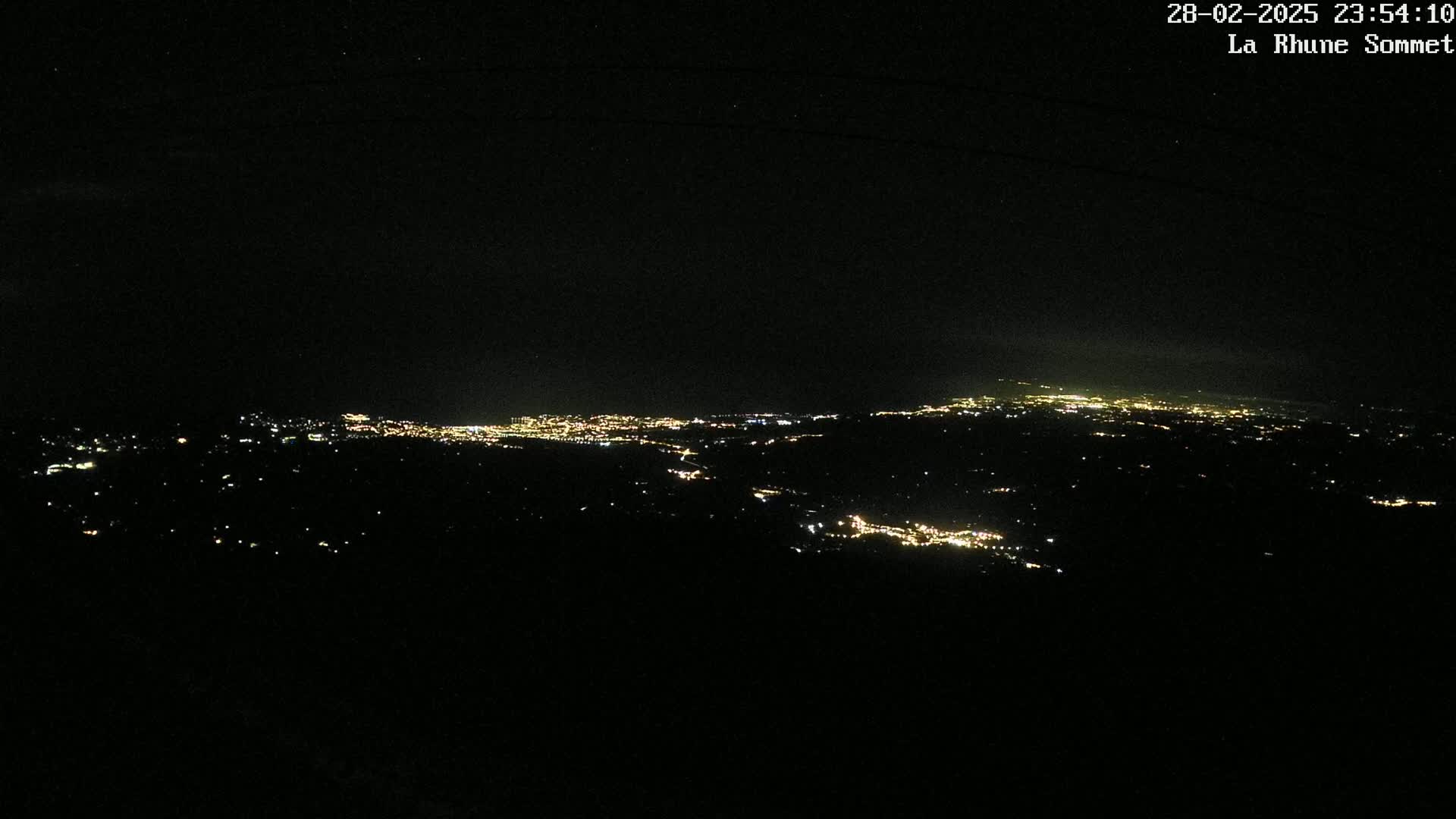 A nighttime, high-angle view shows a sprawling city's lights spread across a dark landscape.