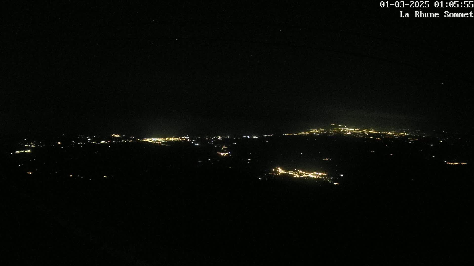A nighttime, high-angle view shows a distant city's lights spread across a dark landscape under a clear, starry sky.